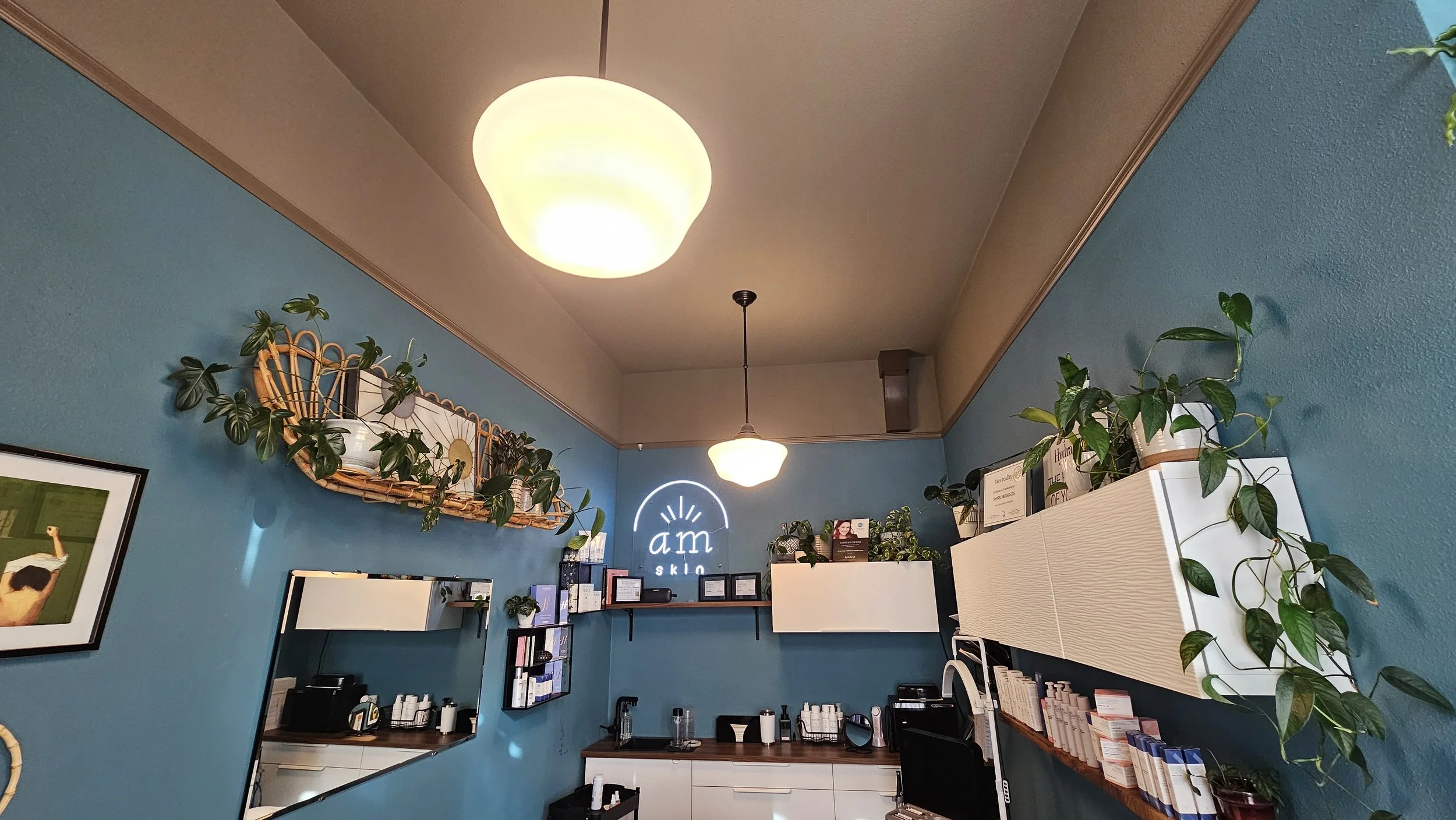 Inside a beauty or skincare salon with blue walls, ceiling lights, shelves with skincare products, and green plants for decoration.