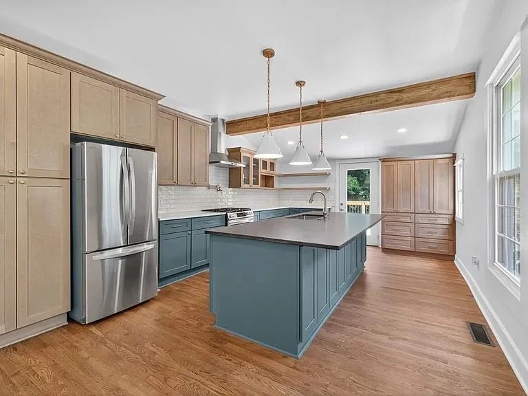 Modern kitchen with a blue island, stainless steel refrigerator, wooden cabinets, and a wooden beam on the ceiling.