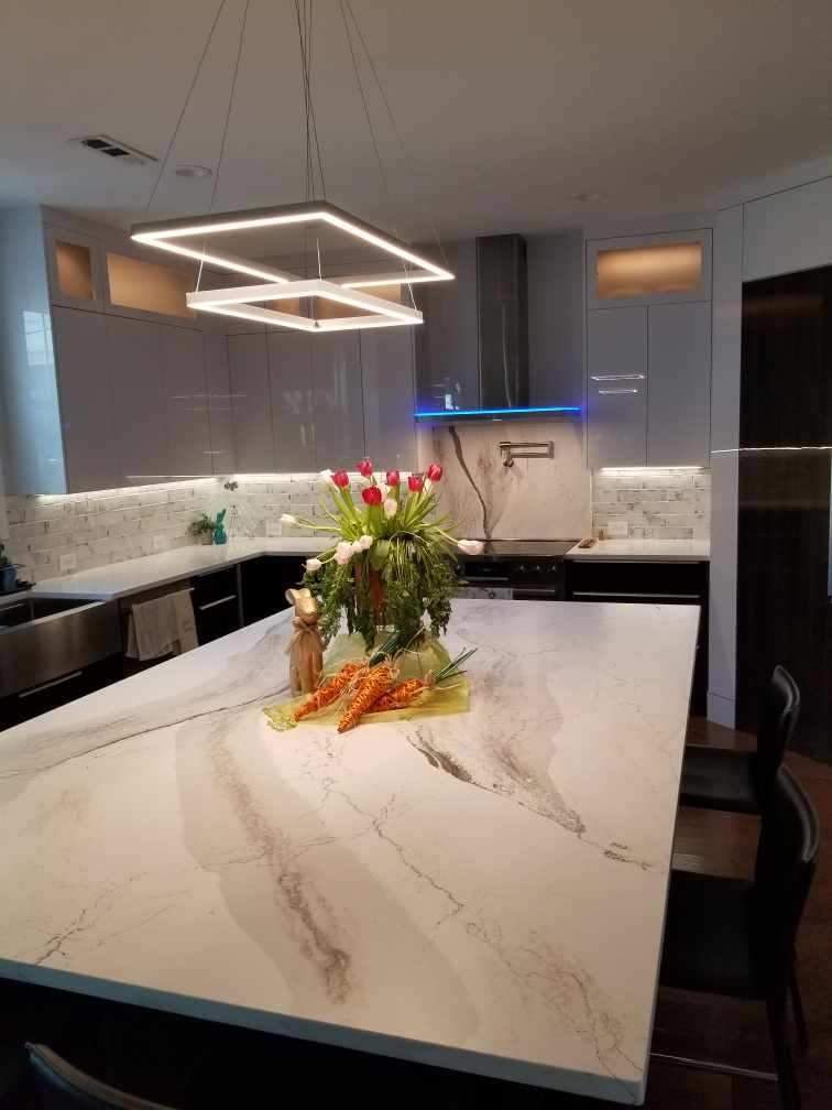Modern kitchen with marble island, floral centerpiece with carrots, gray cabinets, pendant lights, and a stainless steel range hood.
