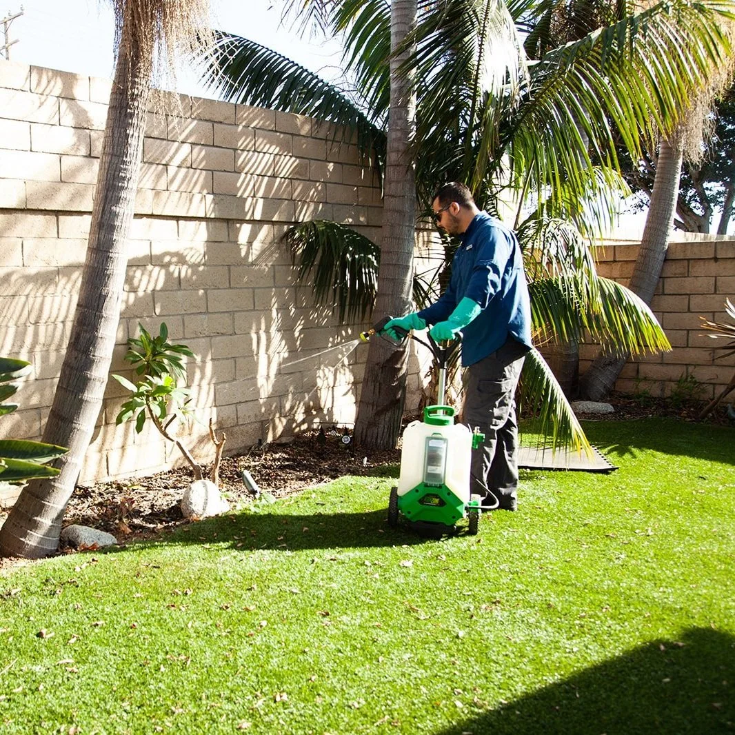 pest control technician applying pesticides with a backpack sprayer on the perimeter wall of a backyard of a residential house.
