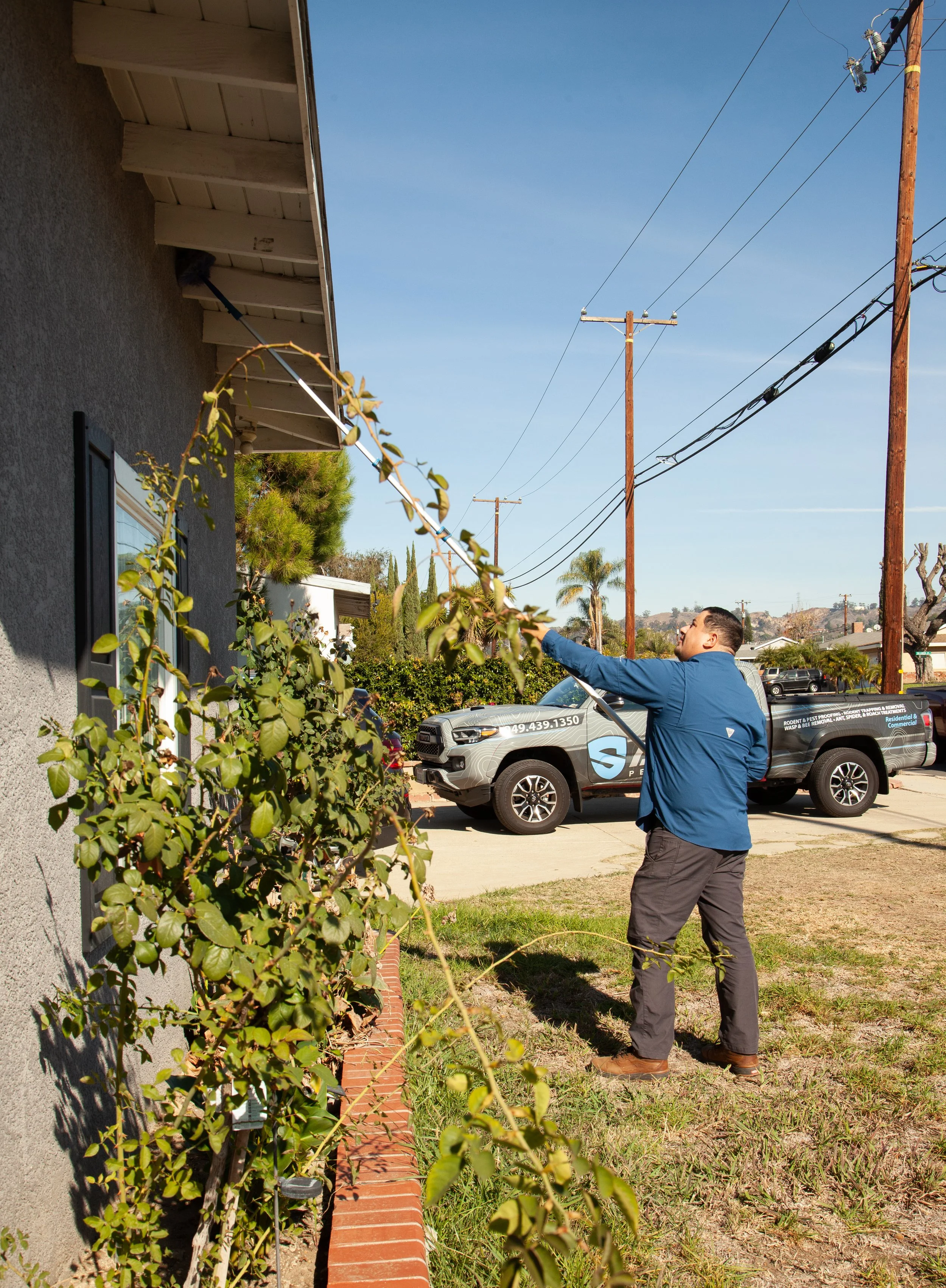 pest control technician using a webber pole to remove webs from the eves of a residential house.