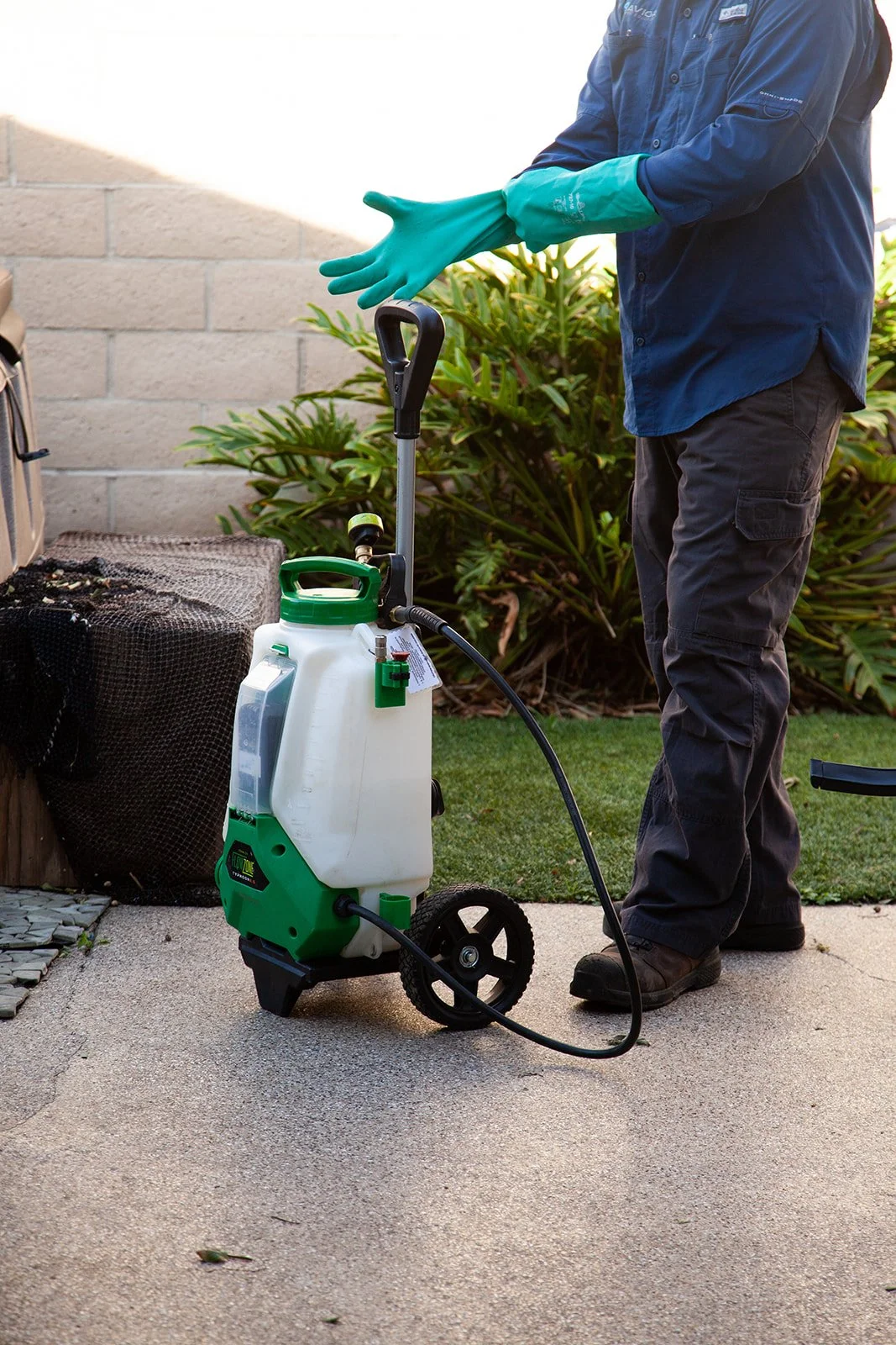 pest control technician getting ready placing his PPE gear or rubber gloves on with backpack sprayer.