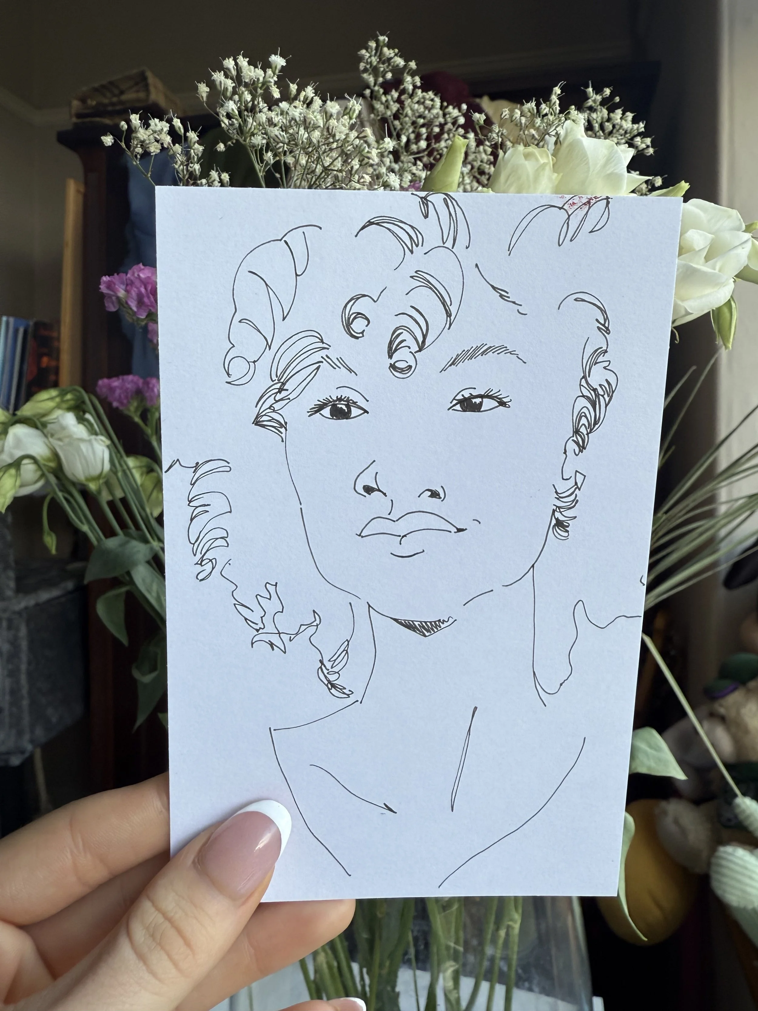 Line drawing of a woman's face on a piece of paper, held in front of a bouquet of flowers.