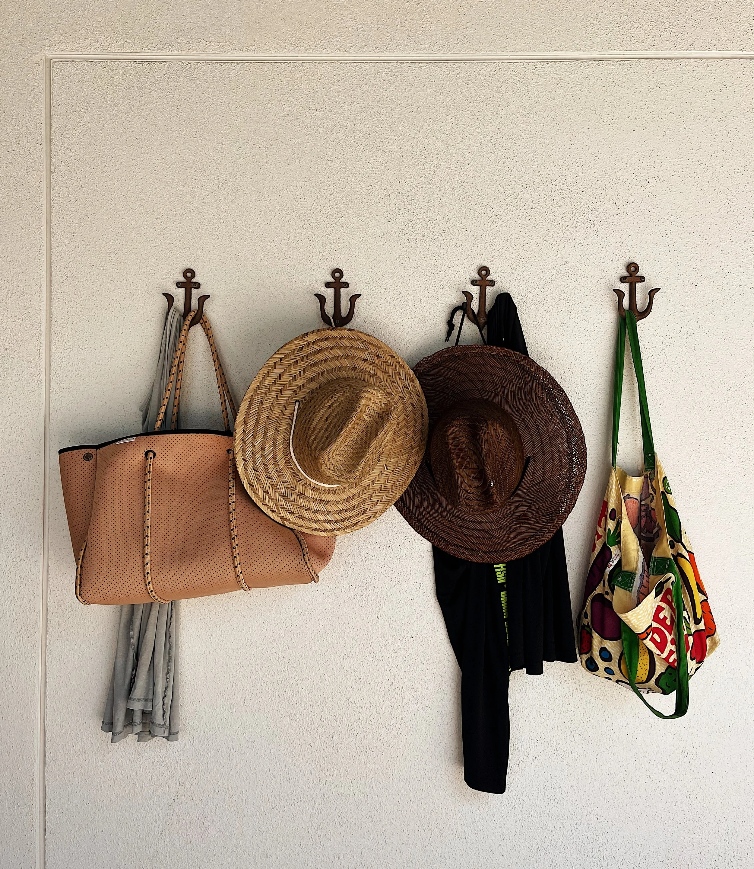 Wall mounted hooks holding a gray skirt, a beige handbag, a straw hat, a dark brown hat, black shorts, and a colorful bag.