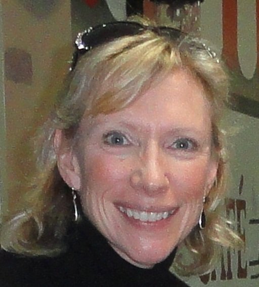 A woman with blonde hair and light skin smiling at the camera, wearing earrings and a black top.