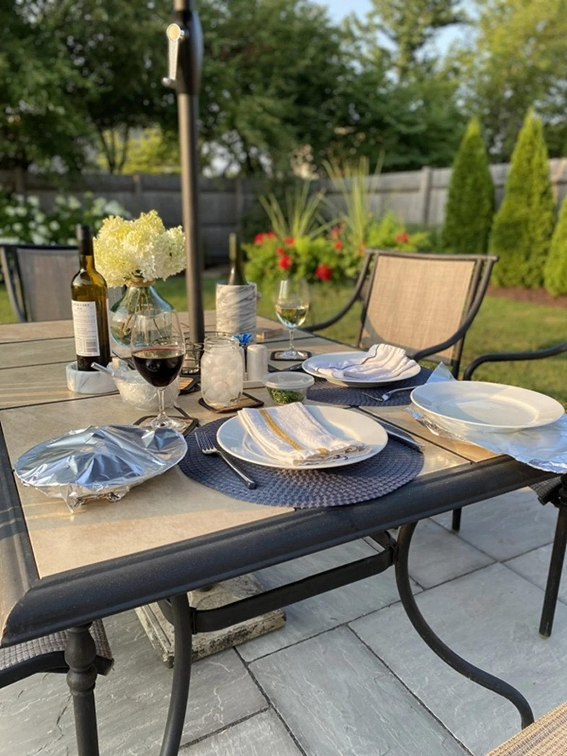 Evening on the Patio: A thoughtfully prepared outdoor table framed by garden greenery and evening light reflects the welcoming atmosphere of al fresco dining and entertaining. This image brings warmth, lifestyle appeal, and a sense of gathering to bo