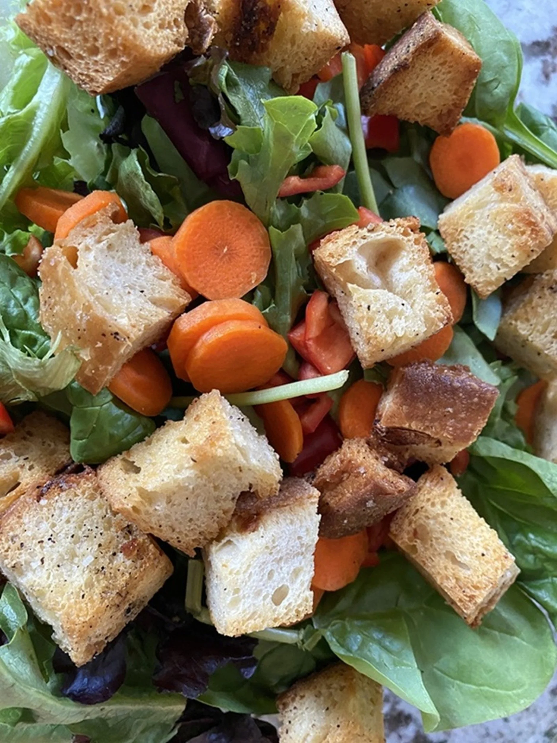 Mixed salad with greens, sliced carrots, cherry tomatoes, croutons, and bread pieces.