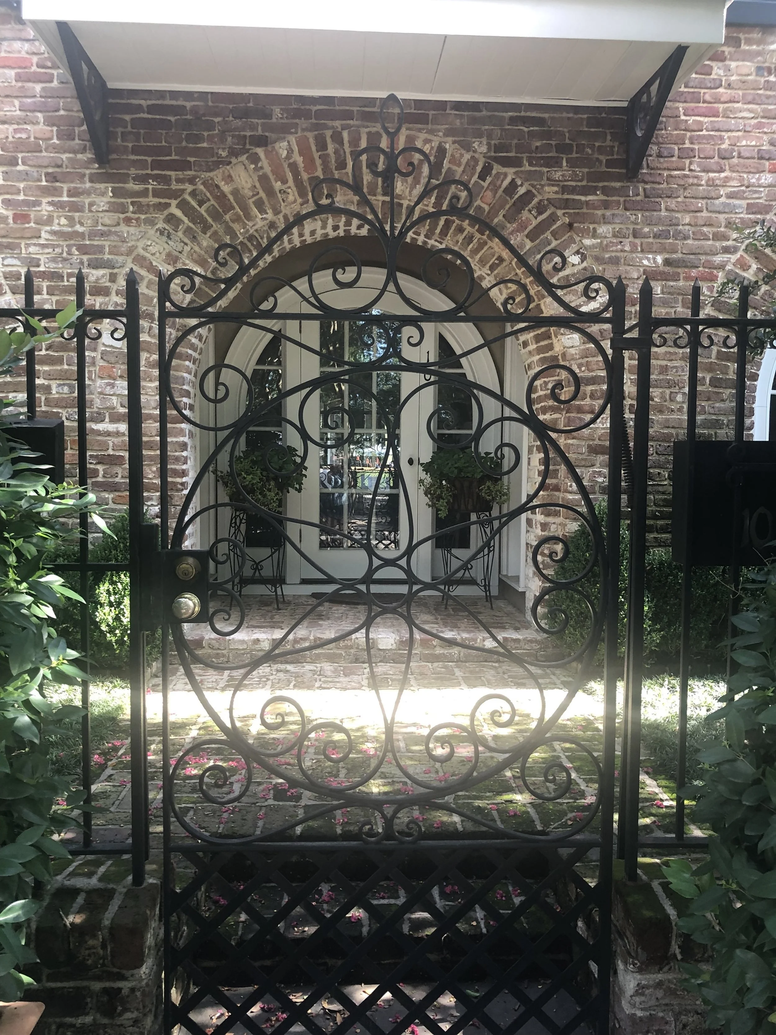 Through the Gate - Charleston Entryway

An ornate wrought iron gate opens into a layered composition of brick, greenery, and soft light. The intricate scrollwork contrasts with the weathered textures behind it, revealing a quiet, curated moment of So