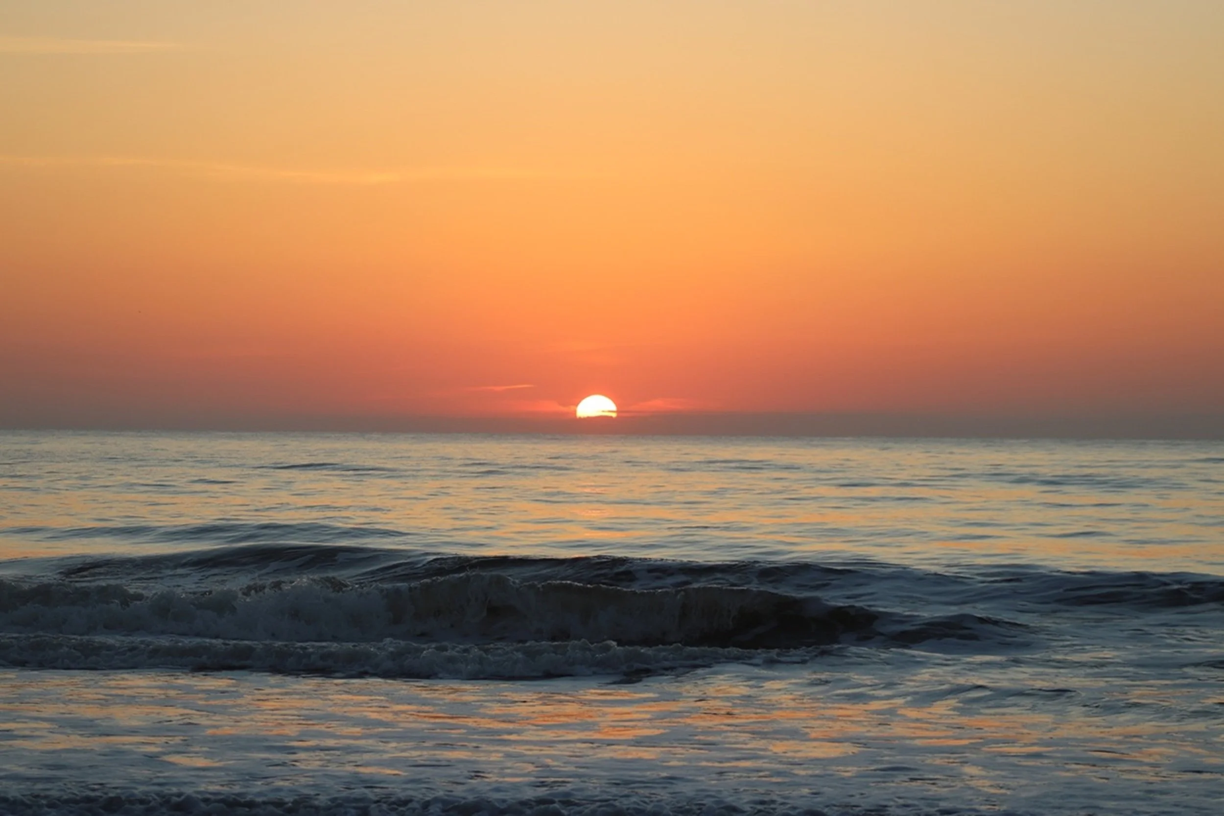 First Rise: The sun lifts above the horizon, casting soft amber light across gentle ocean swells in a timeless coastal scene. With its understated elegance and soothing palette, this image brings warmth and serenity to guest suites, spa retreats, and
