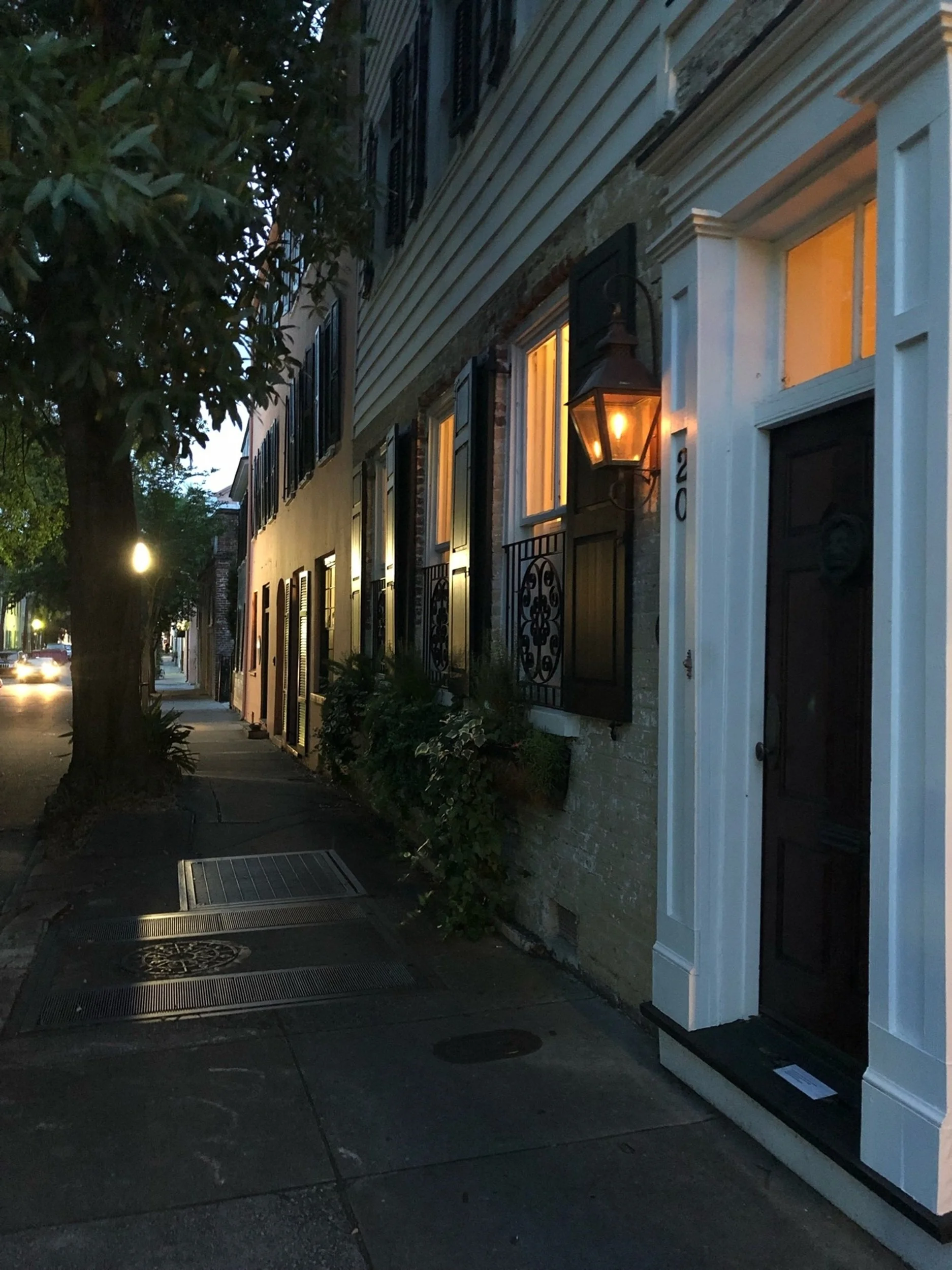 Lanterns at Dusk: Historic facades and glowing lanterns line a quiet Charleston street as evening settles across the city. The warm illumination and intimate atmosphere create a sense of welcome and timeless Southern hospitality, making this image id
