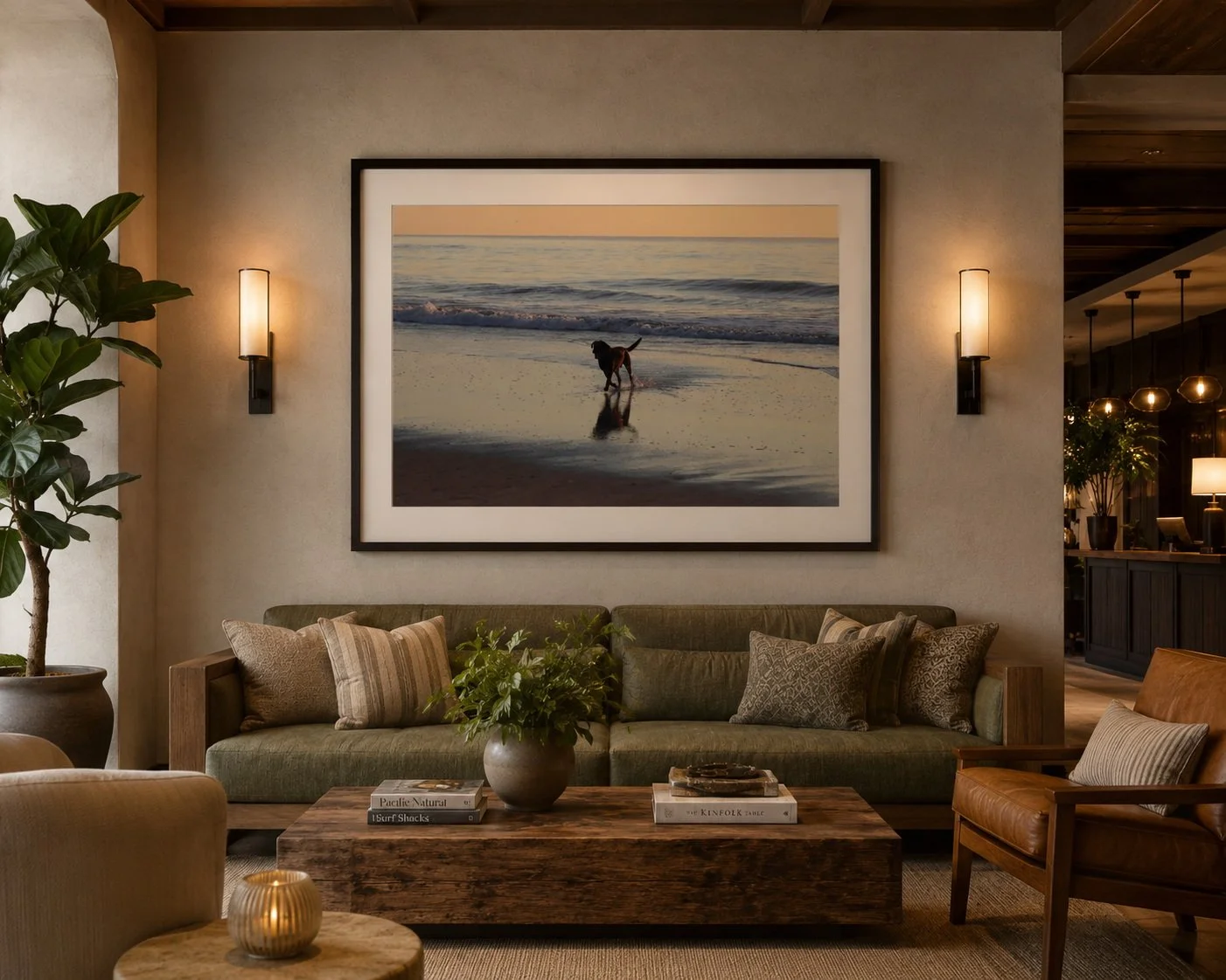 Living room with green sofa, wood coffee table, framed beach photo, dog photo on beach, indoor plants, wall sconces, and warm lighting.