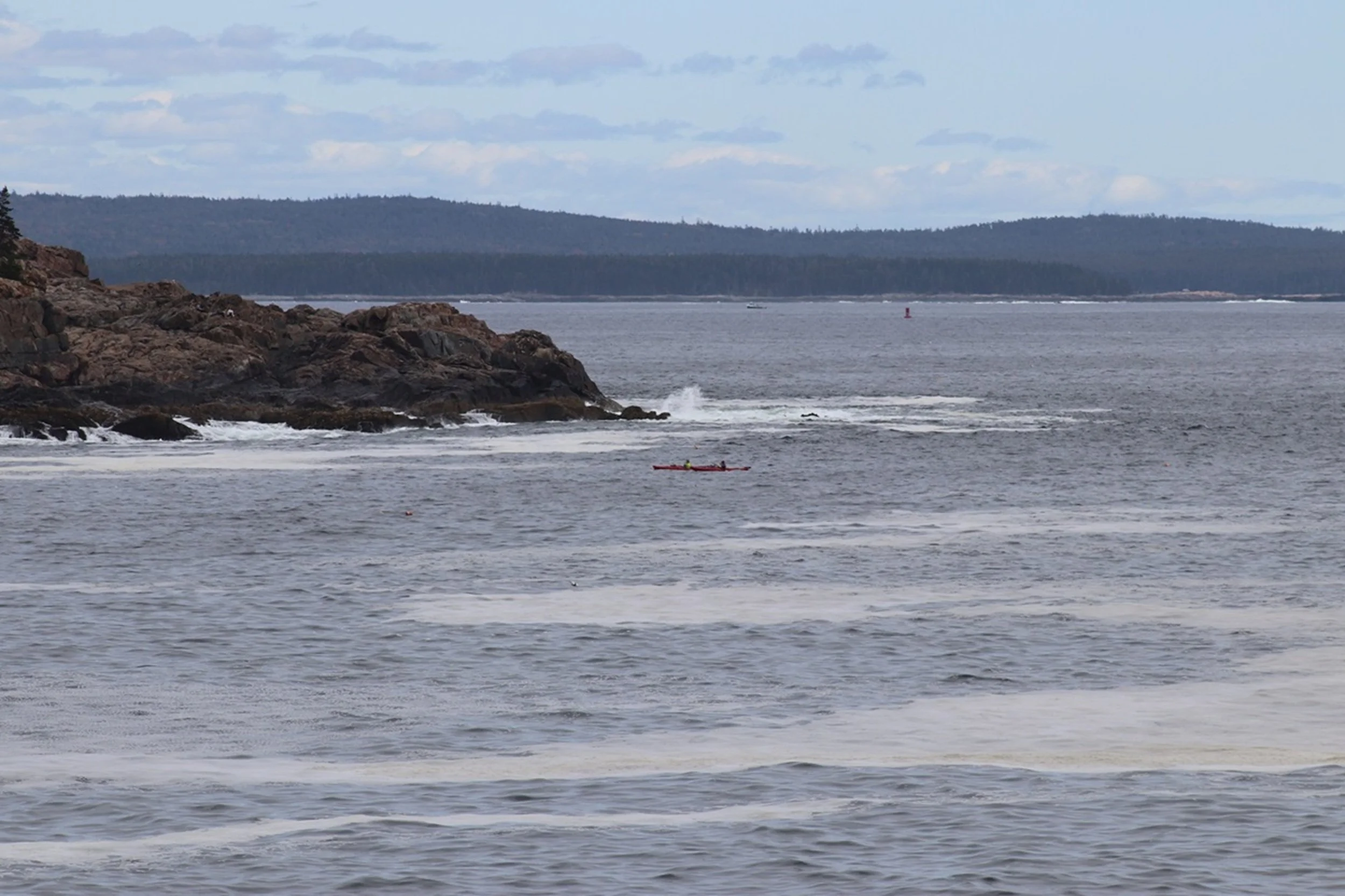 Red Kayak in Open Water - Penobscot Passage: A lone red kayak cuts across open coastal waters against a backdrop of distant islands and rugged shoreline, evoking a compelling narrative of exploration and adventure. This image brings a sense of freedo