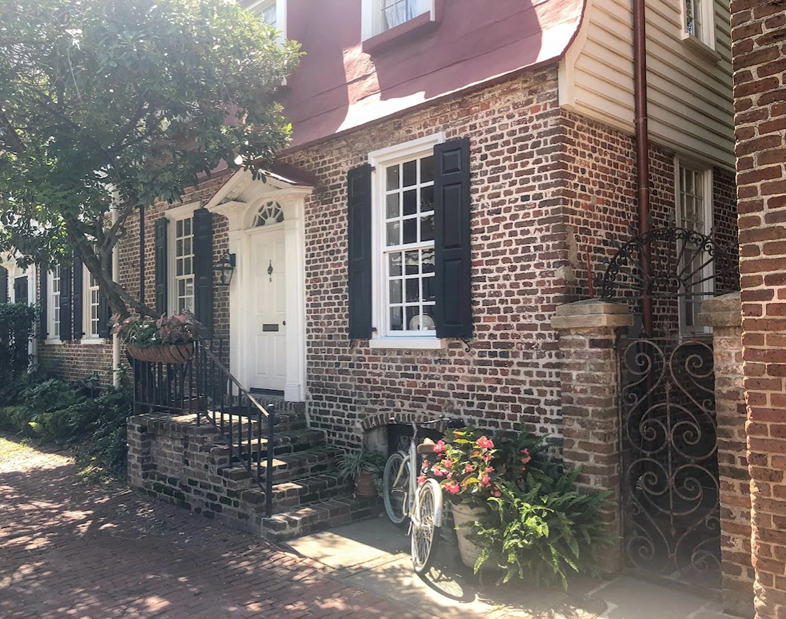 Brick and Welcome

A sunlit brick façade with black shutters, wrought iron railings, and a simple white doorway framed by flowering planters. A bicycle rests quietly below the window, adding a lived-in charm to this historic streetscape.

Warm brick 
