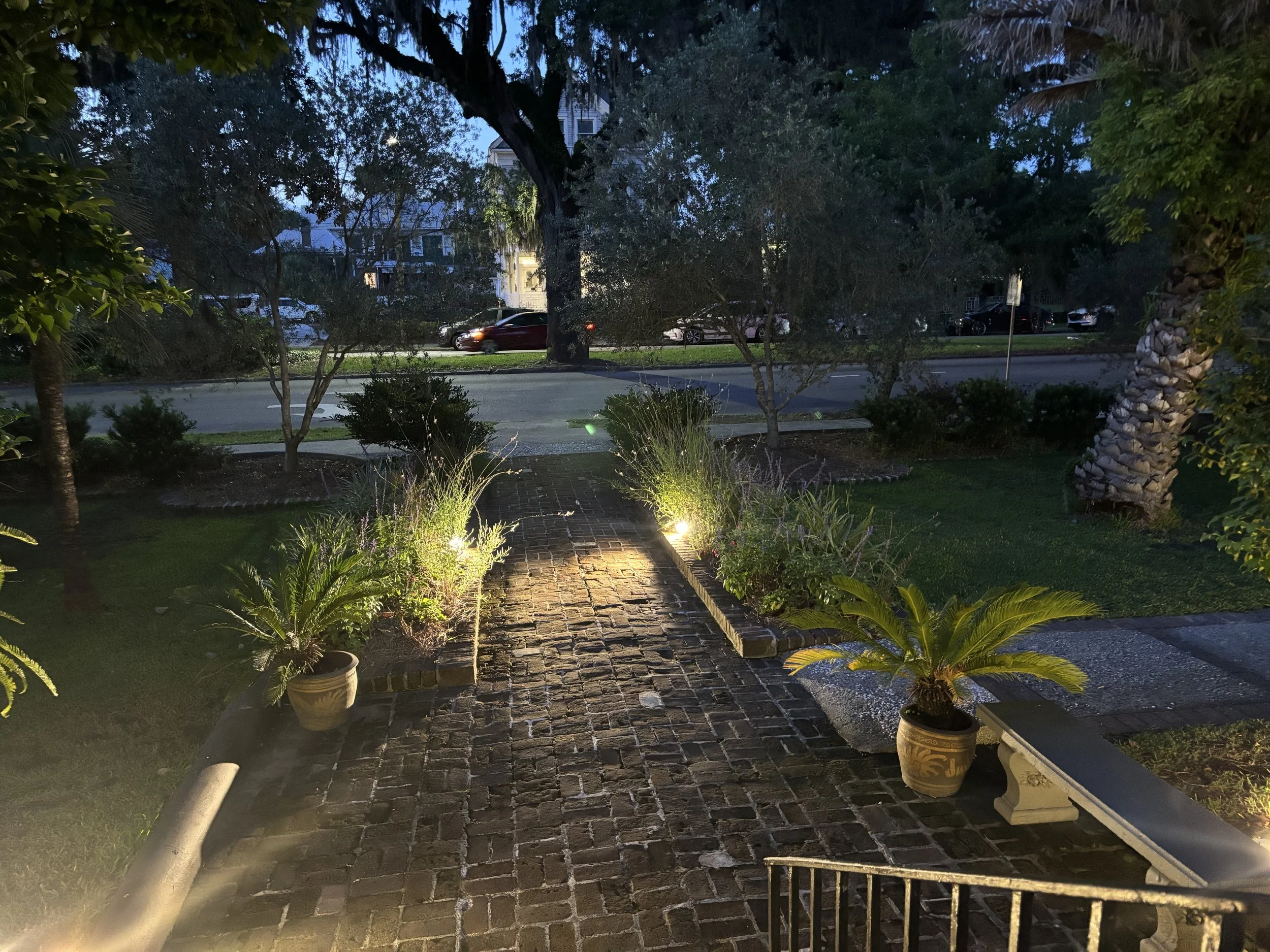 Evening Arrival: A softly illuminated brick pathway welcomes guests with warmth, elegance, and a quiet sense of anticipation. Framed by lush Southern landscaping and gentle architectural lighting, Evening Arrival captures the transition between day a