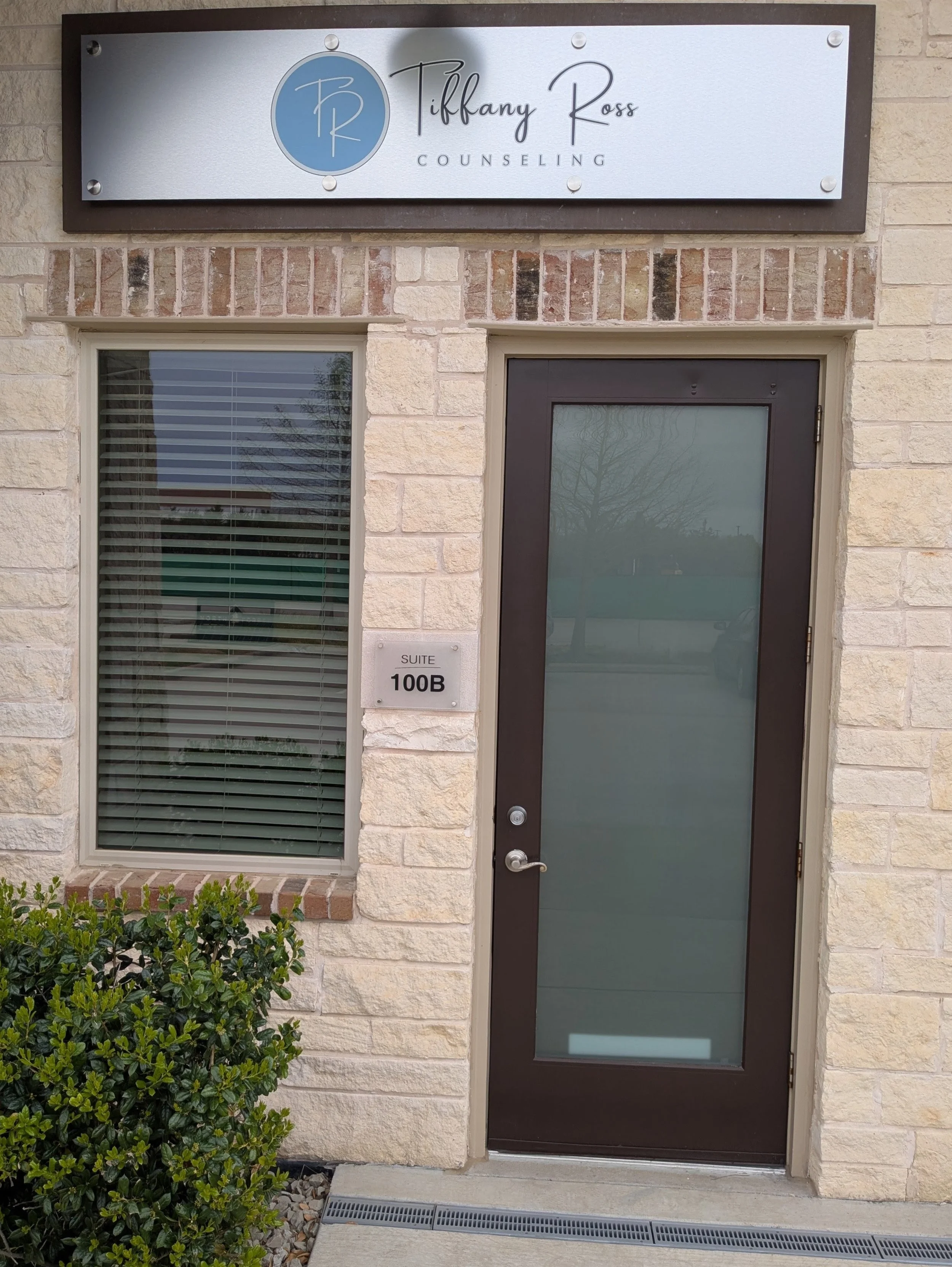 Sign for Tiffany Ross Counseling office above the entrance door. The office is located at suite 100B, with a window and bushes in front of the building.