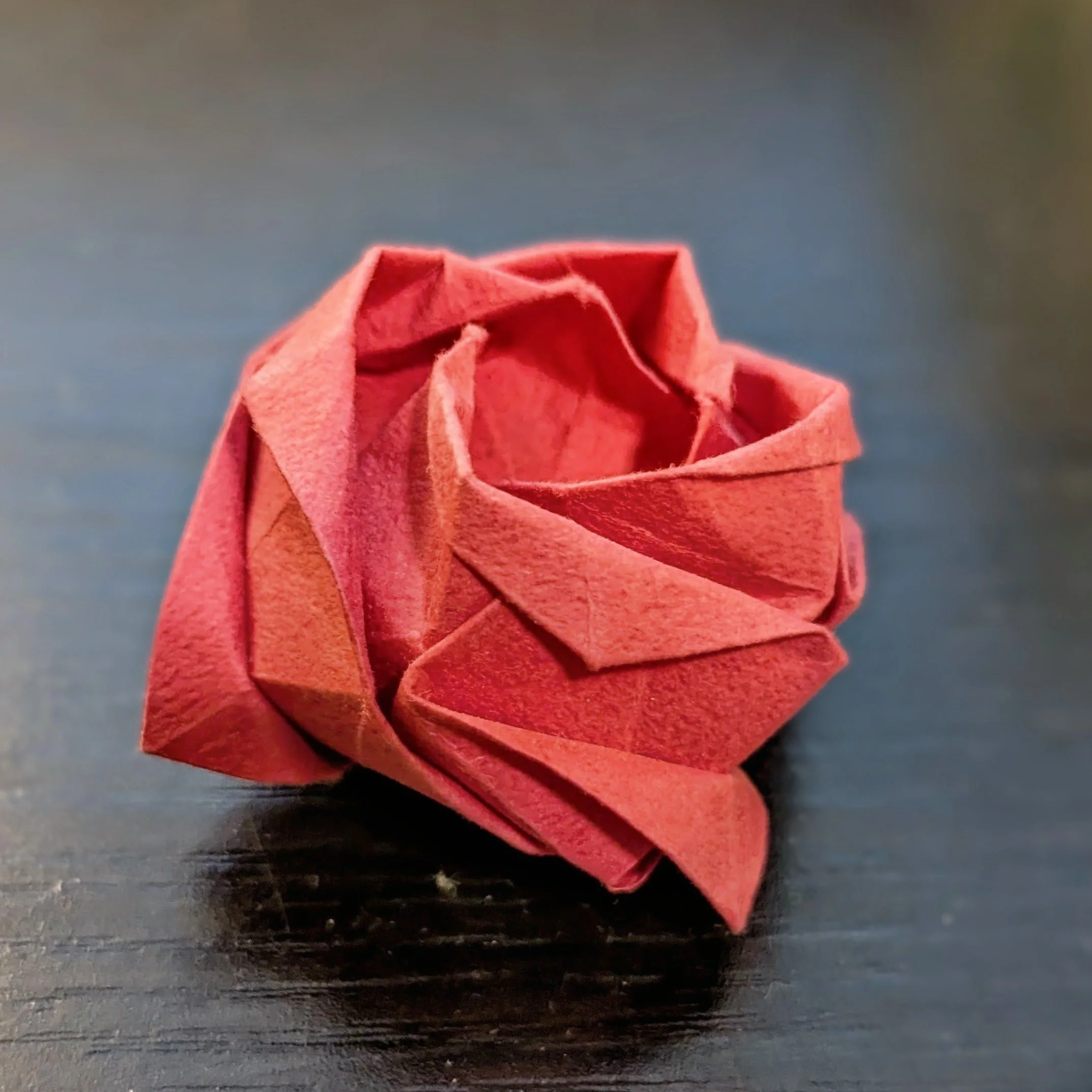 A close-up of an orange origami paper flower resting on a dark surface.