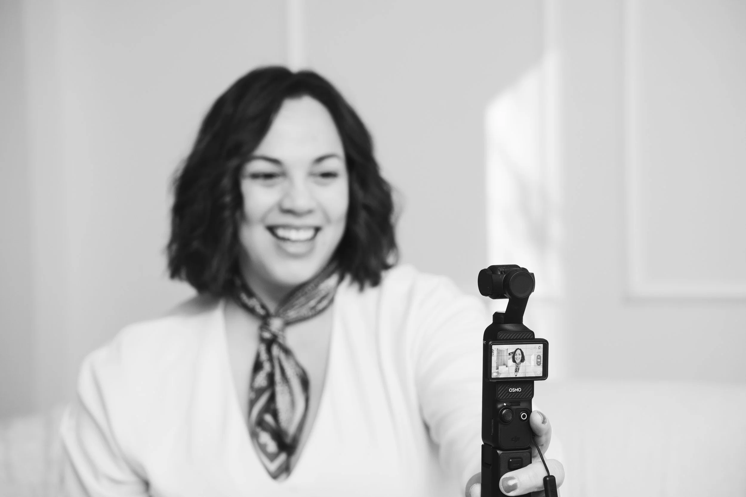 Mujer sonriendo y tomando una selfie con un estabilizador de cámara en un entorno interior.