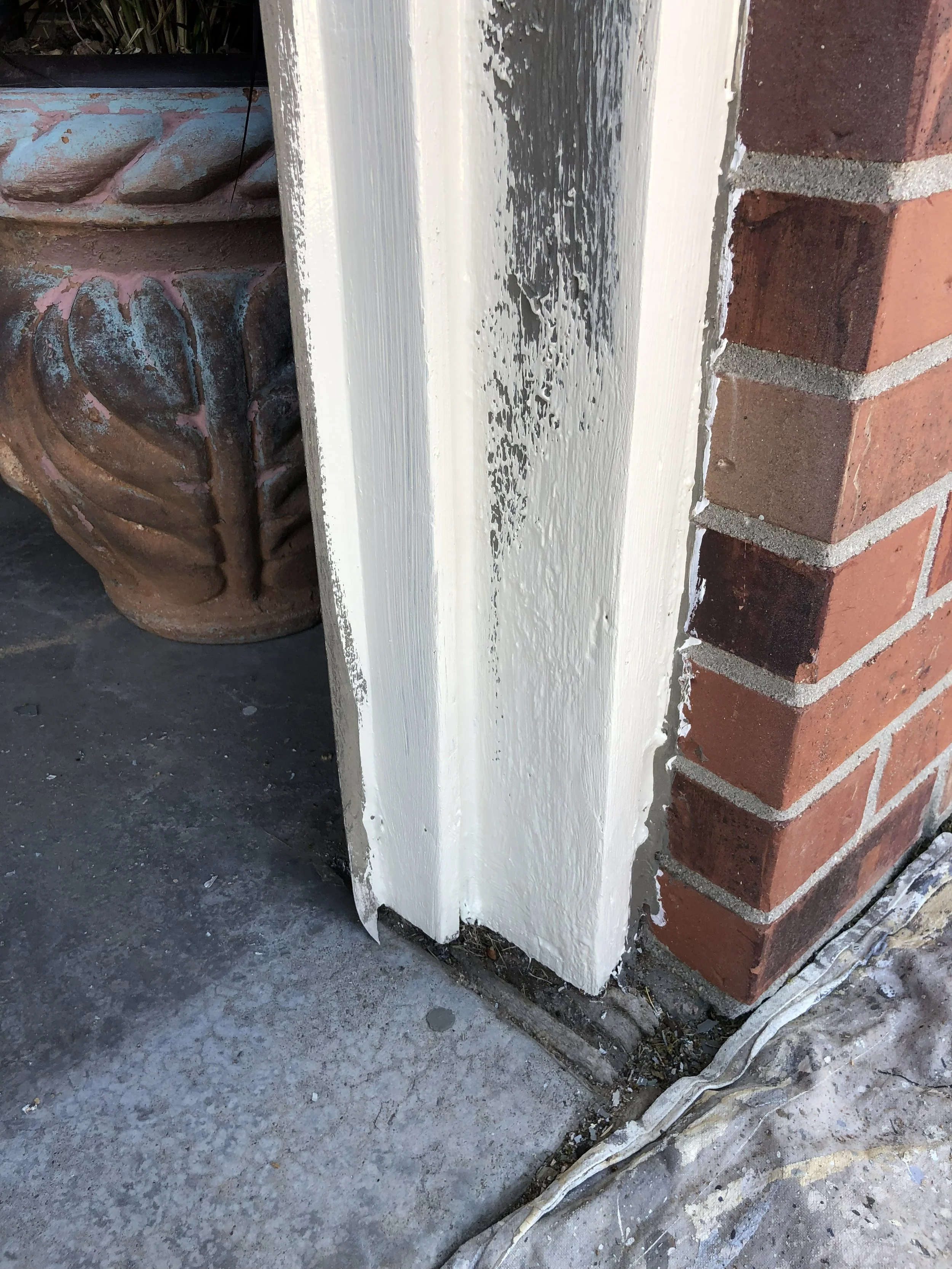 Close-up of a corner of a brick building with a white painted wooden trim and electrical cables on the ground.