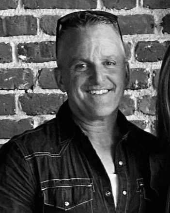 Black-and-white photo of a man smiling with a brick wall background.