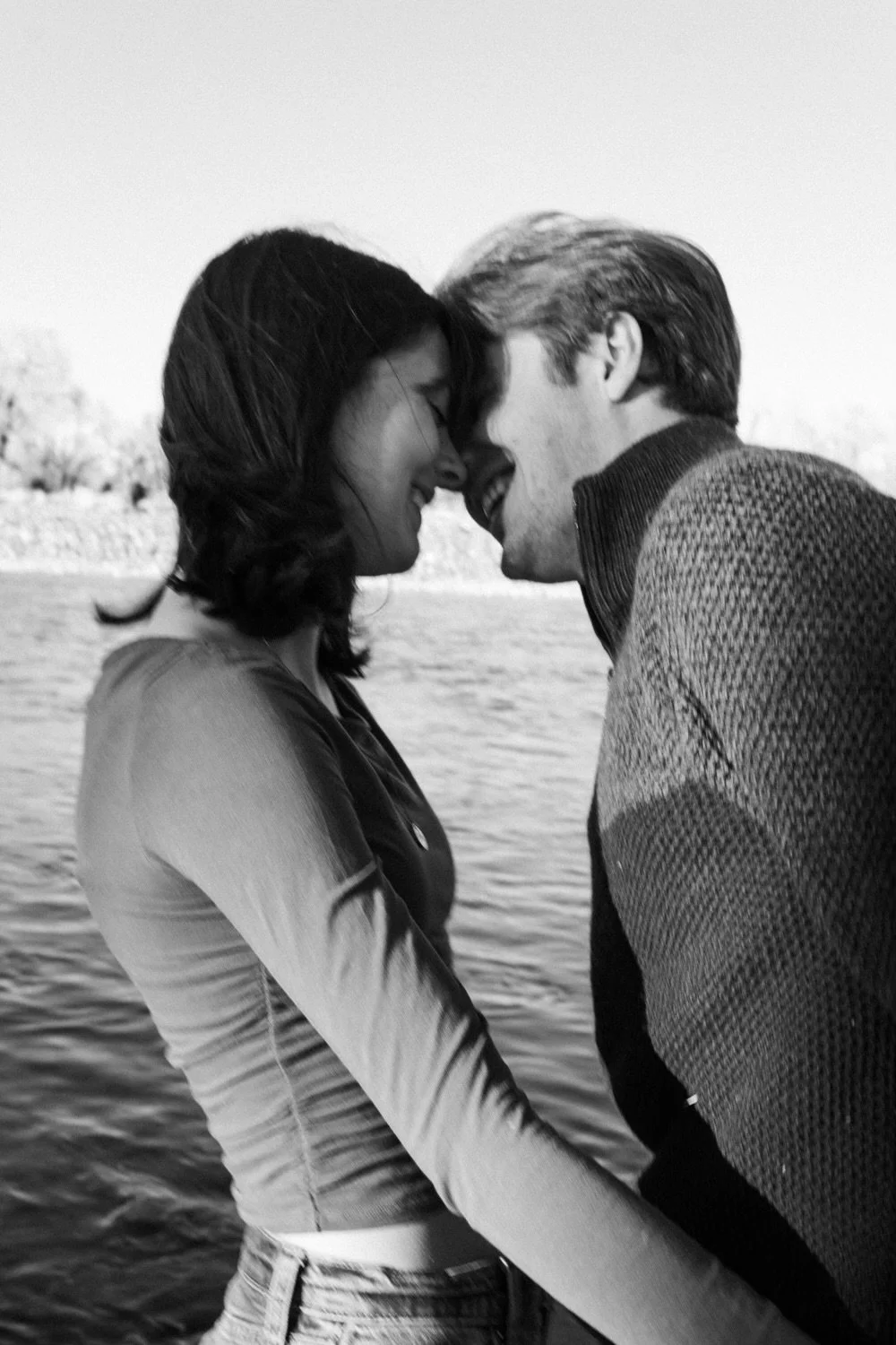 A black and white photo of a couple with foreheads touching, smiling, near a river, outdoors. Paradise Valley, Montana cinematic film couples photography. Engagement photography in St. Augustine, Florida, Montana, and South Dakota. Beach engagement.