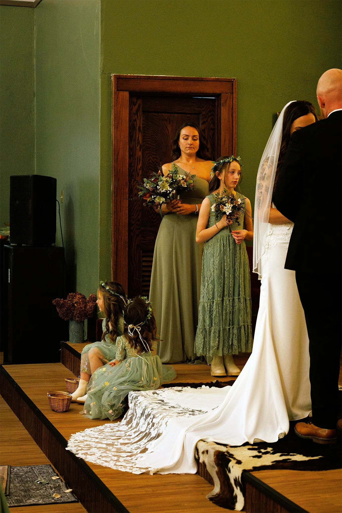 A wedding ceremony scene at the al. Two flower girls sit on the stage, holding baskets and wearing flower crowns. A bride and groom stand at the altar. Intimate image of western ceremony. Couples photography in St. Augustine, FL, Montana.