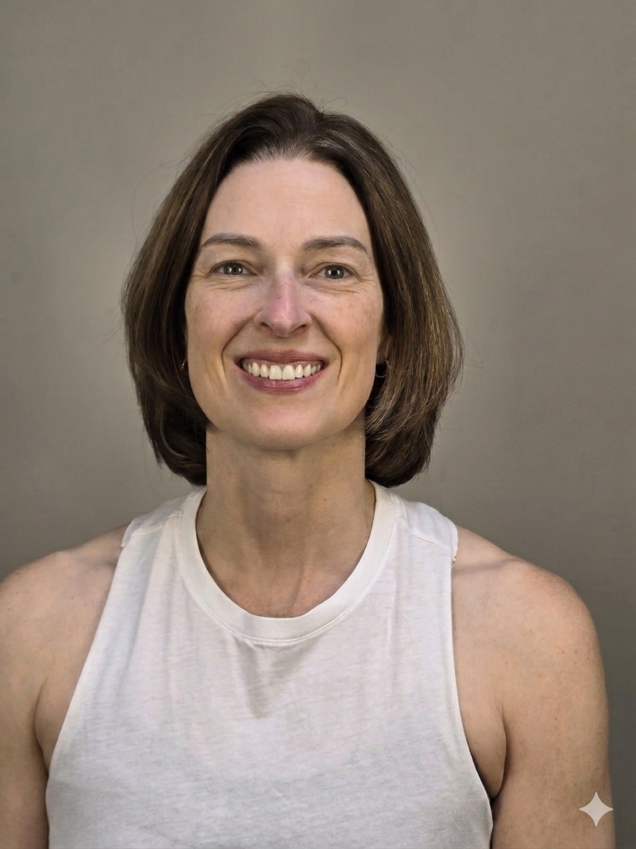 A woman with shoulder-length brown hair smiling and wearing a sleeveless white top, standing in front of a plain gray background.