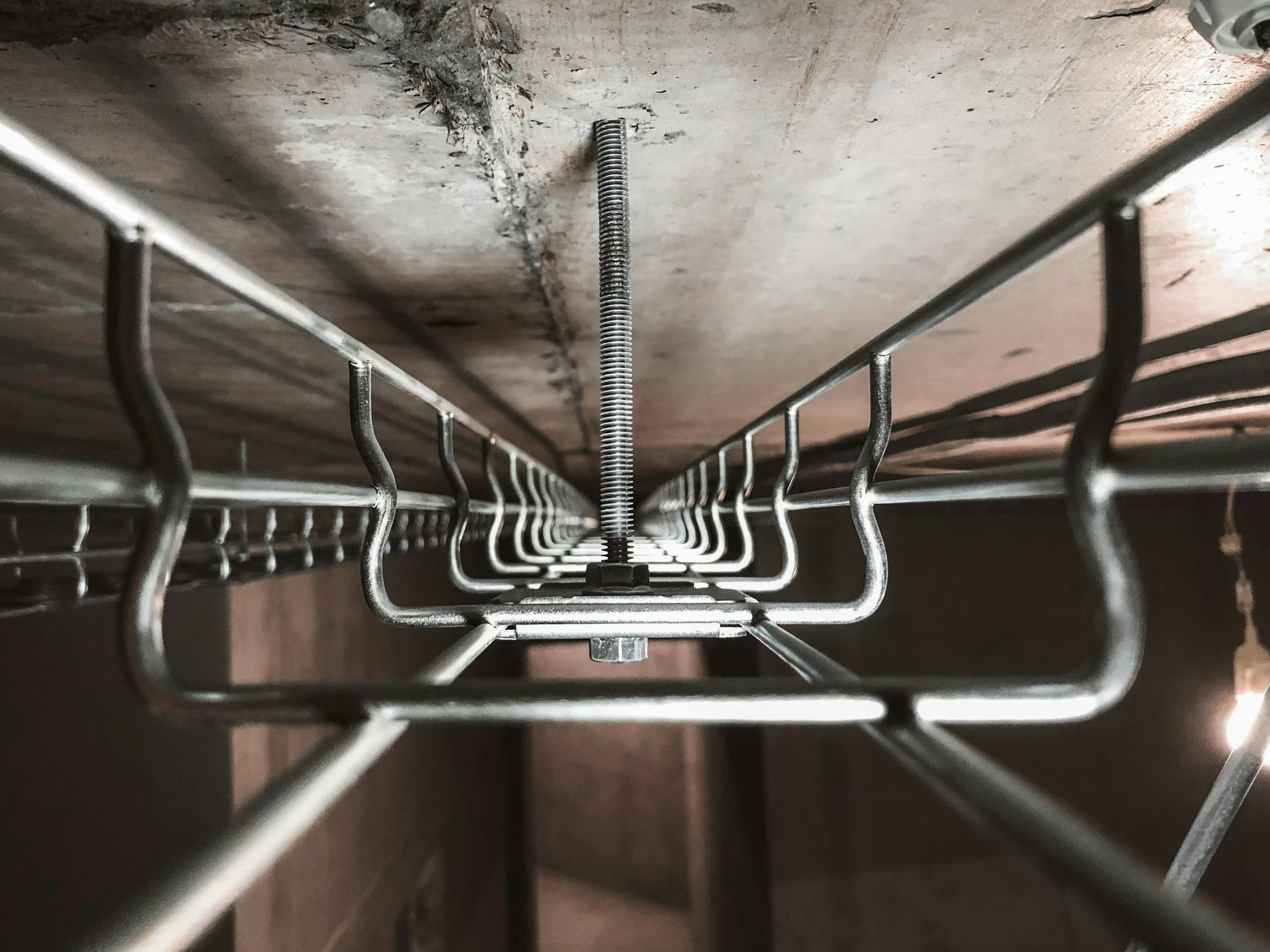 Close-up view of metal wire racks attached to a concrete ceiling, secured with a central bolt and nut.