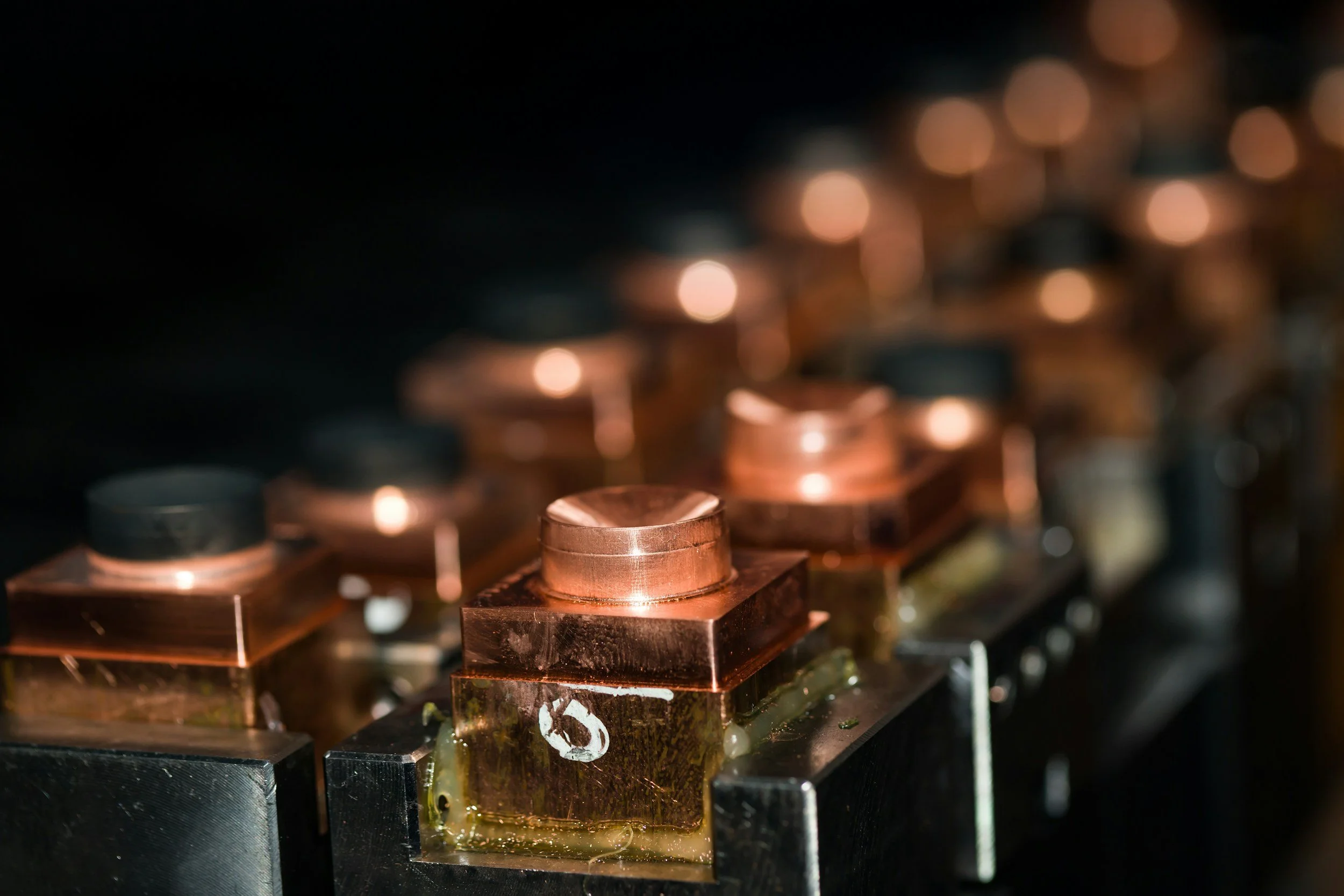 Close-up of shiny copper coils and metal components with molten solder and green flux on a circuit board.