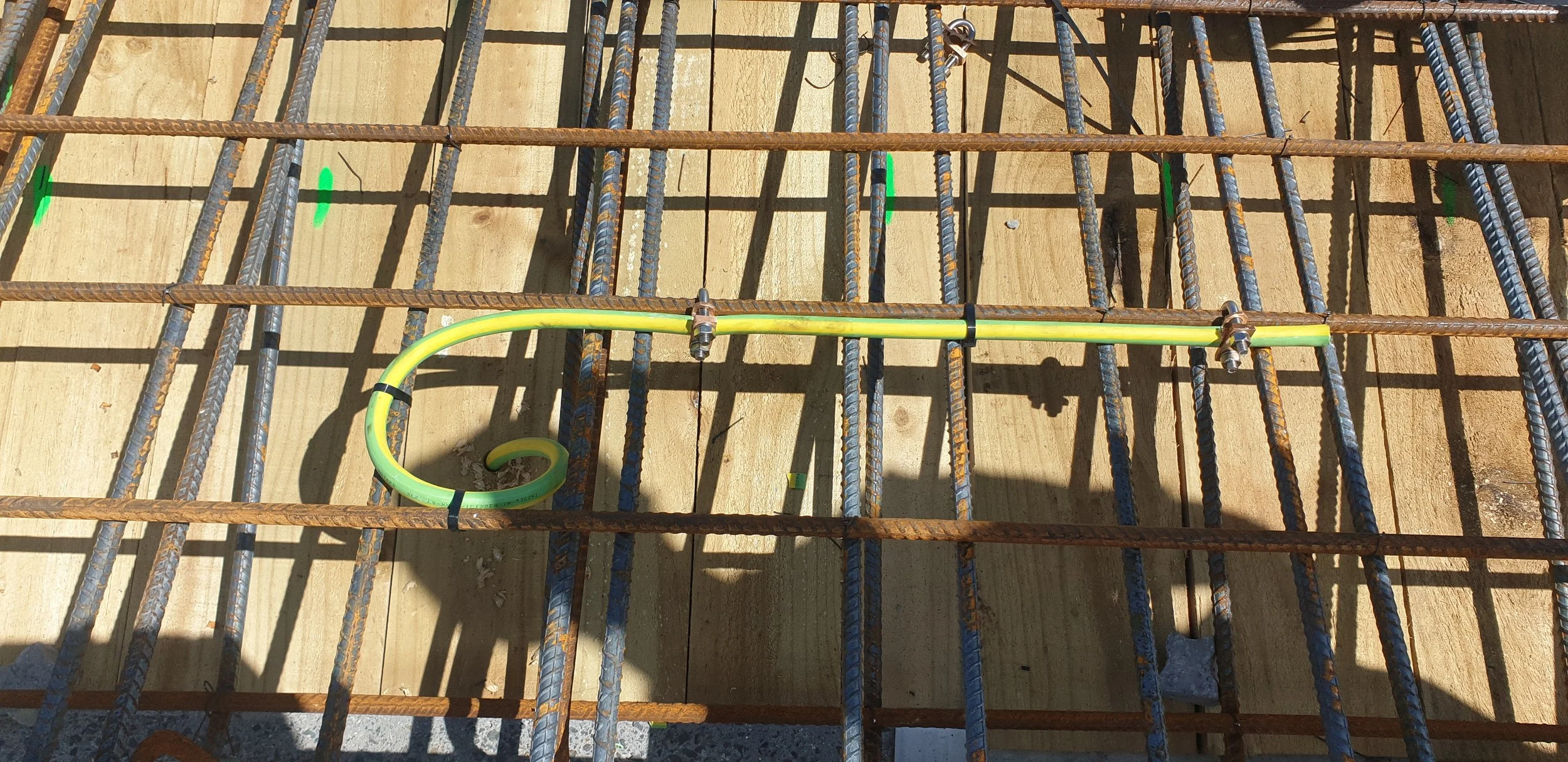 Steel rebar grid on a concrete foundation with a yellow flexible conduit and green spray paint marks.