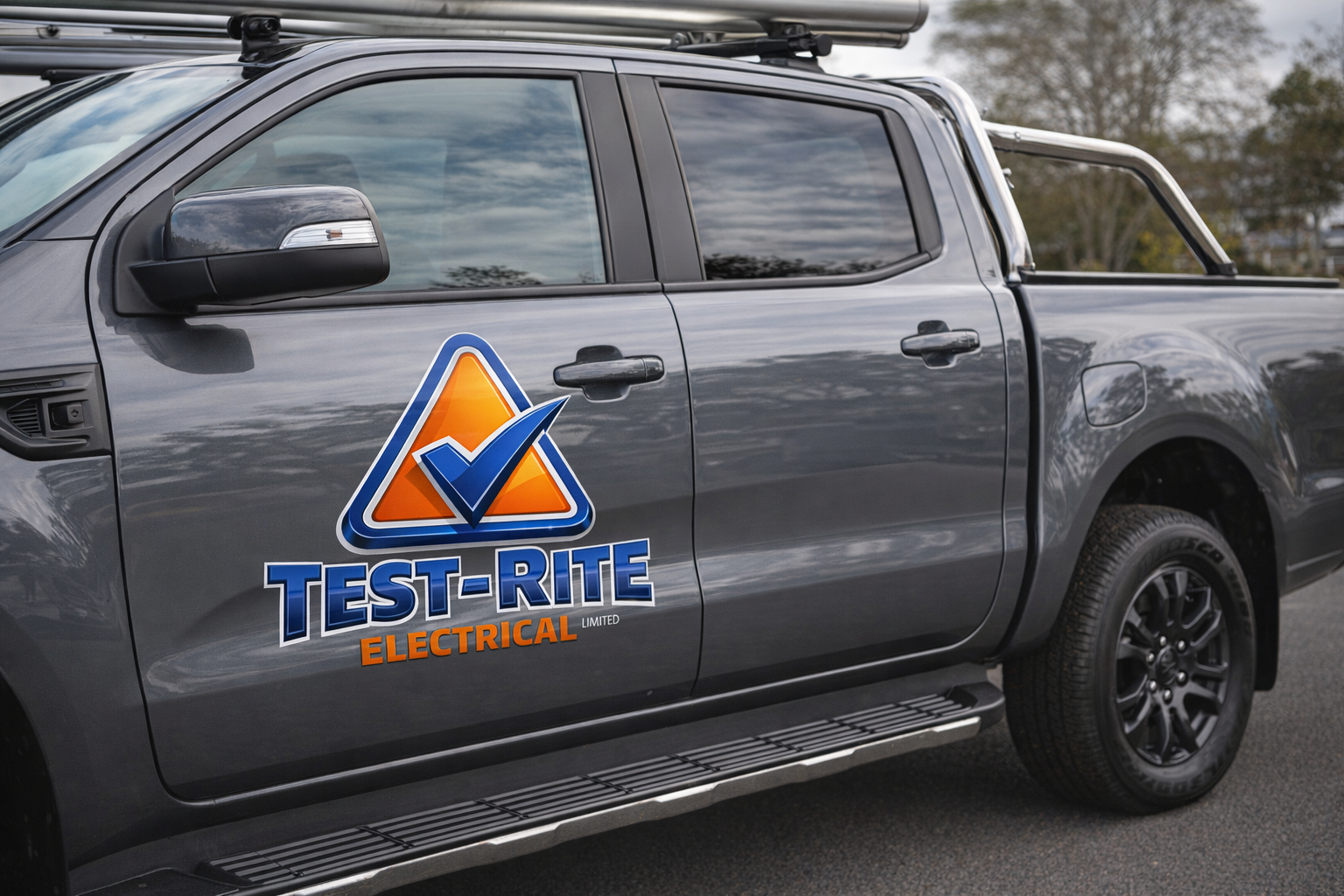 A gray pickup truck with the logo of Test-Rite Electrical Limited, featuring a blue check mark inside an orange triangle, on the door.