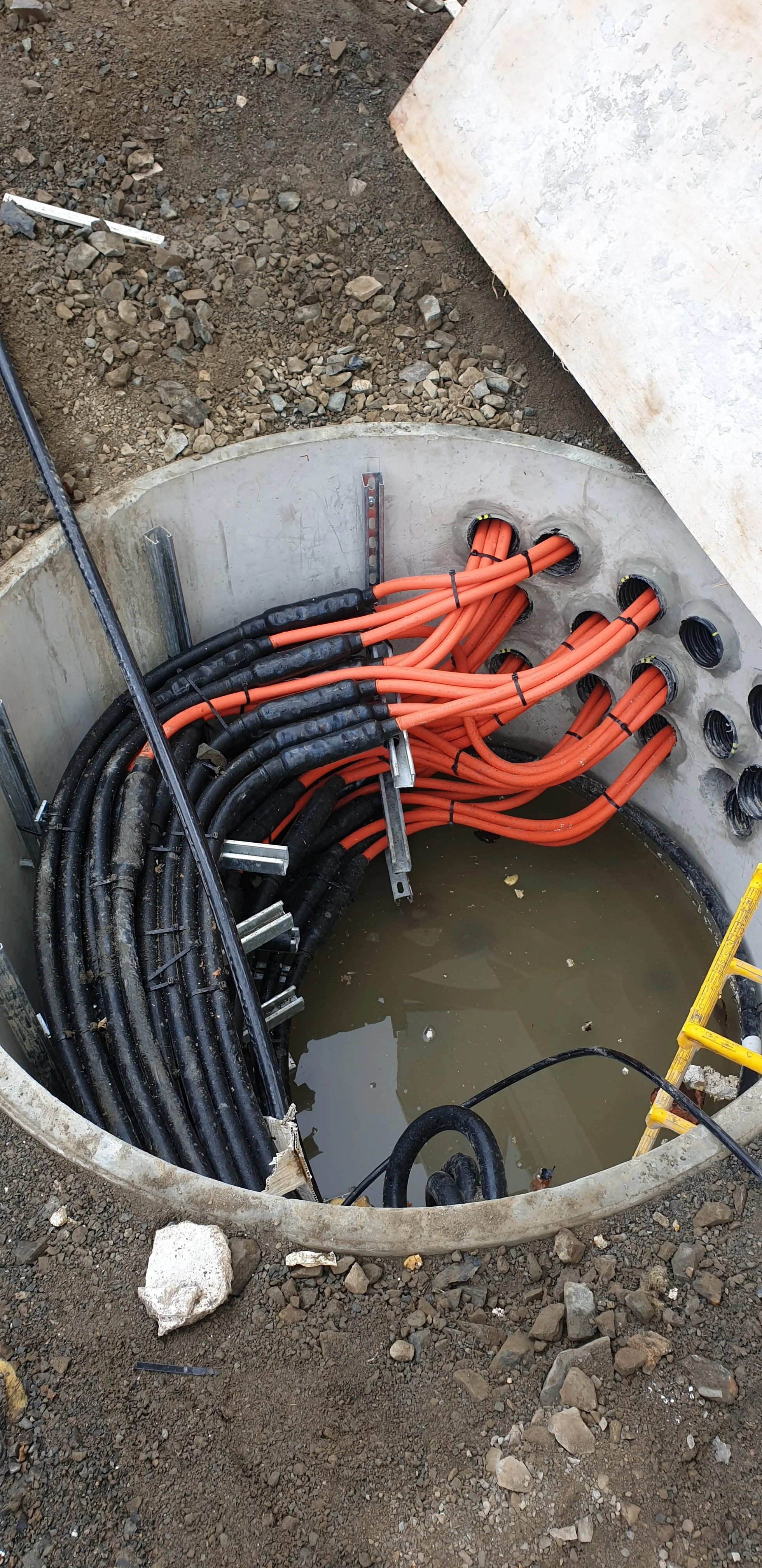 Electrical cables and conduits installed in a circular concrete underground utility vault filled with water at a construction site.