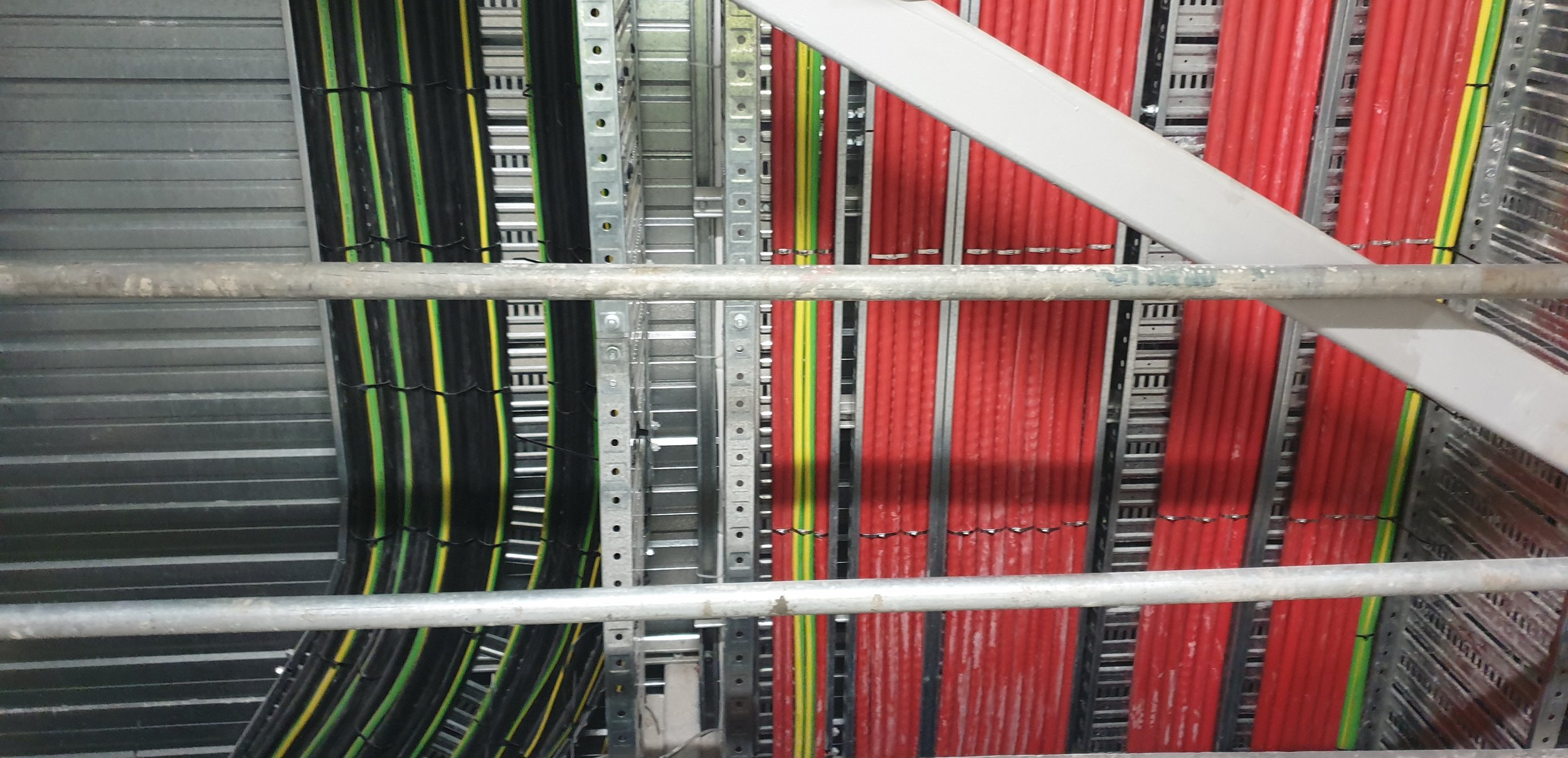 Inside a server room with black and red network cables organized on racks, with metal framing and a gray background.
