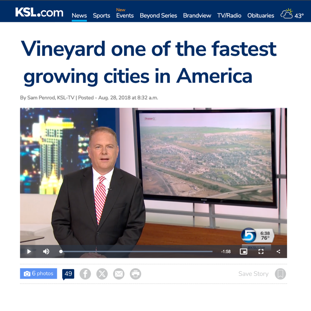 A KSL5 news broadcast featuring a male news anchor in a suit standing in front of a large screen displaying an aerial view of a cityscape. The title on the screen reads, "Vineyard one of the fastest growing cities in America."