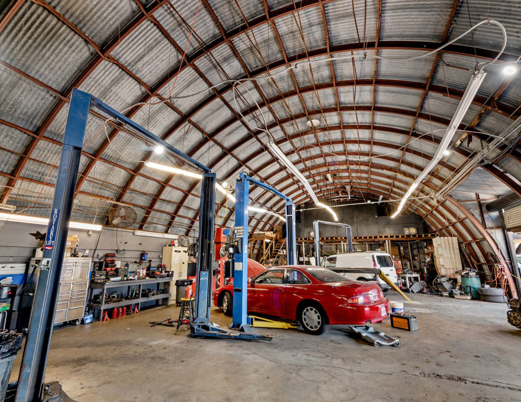 Inside an automotive repair shop with a red car on a lift, various tools, and equipment.
