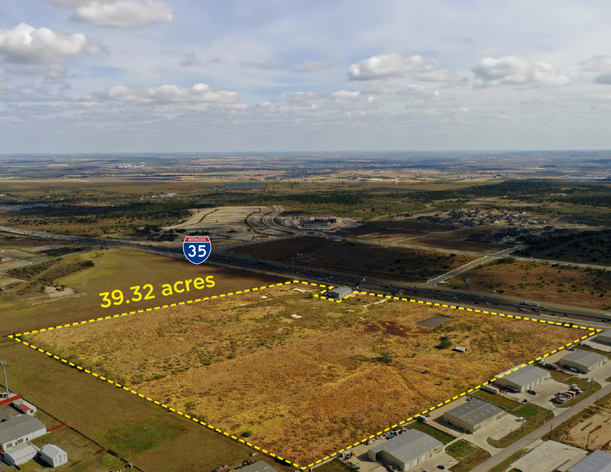 Aerial view of a large vacant plot of land measuring 39.32 acres, outlined with yellow dashed lines, situated near Interstate 35 in a semi-urban area with residential neighborhoods, roads, and some industrial buildings, under a partly cloudy sky.