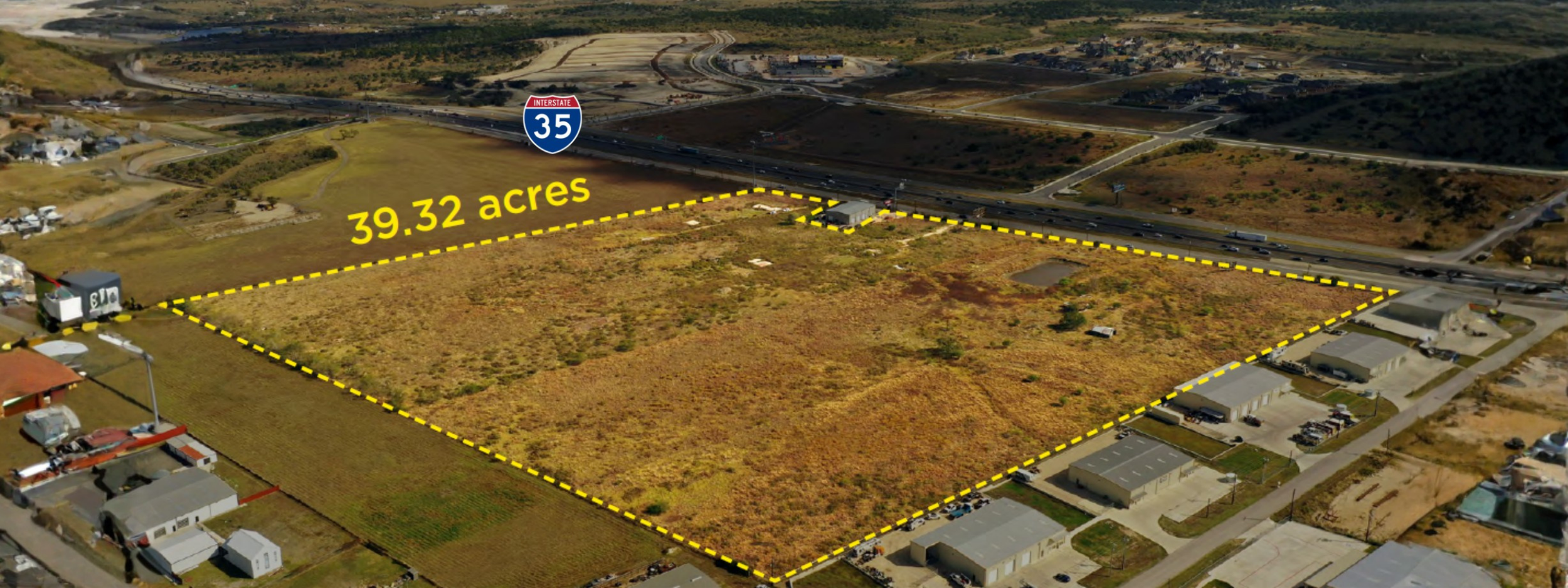 Aerial view of a large undeveloped plot of land measuring 39.32 acres, marked with yellow dashed lines, near Interstate 35 in a suburban area with residential buildings and a busy highway.