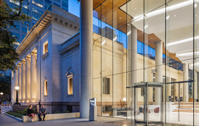 Modern building with glass exterior, large columns, and classical architectural elements, with people sitting on benches outside.