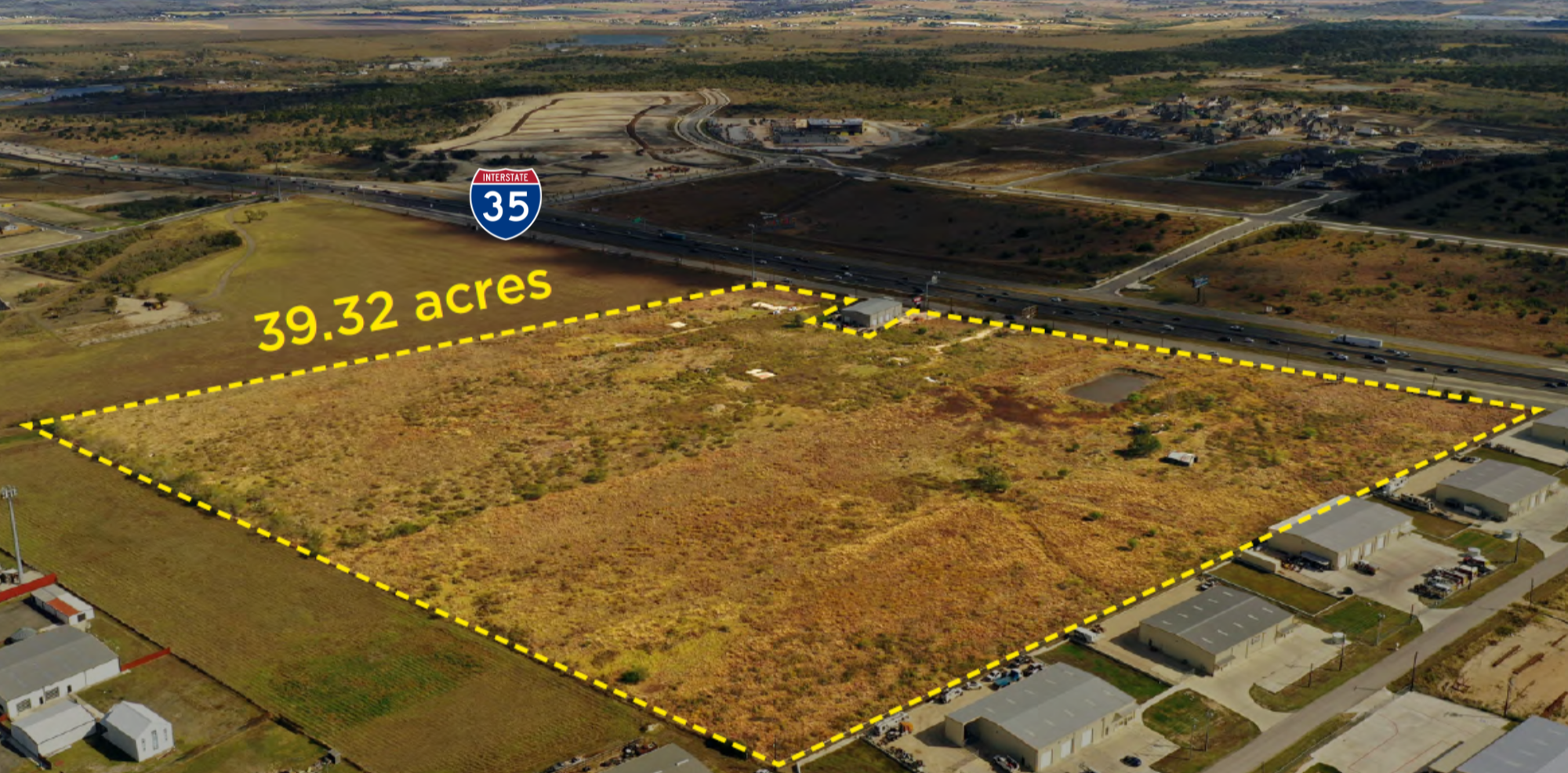 Aerial view of a 39.32-acre plot of undeveloped land situated near Interstate 35 with residential and commercial buildings nearby, bordered by roads and some scattered structures.