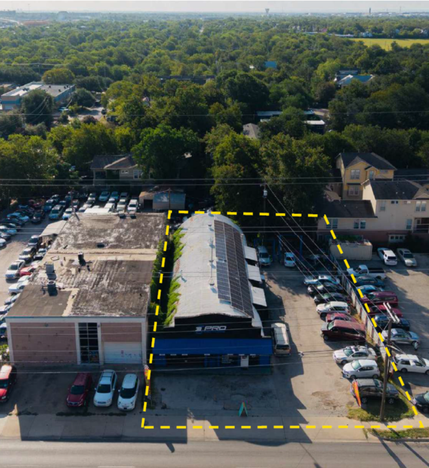 Aerial view of a parking lot and adjacent buildings, one with solar panels on the roof, outlined in yellow.