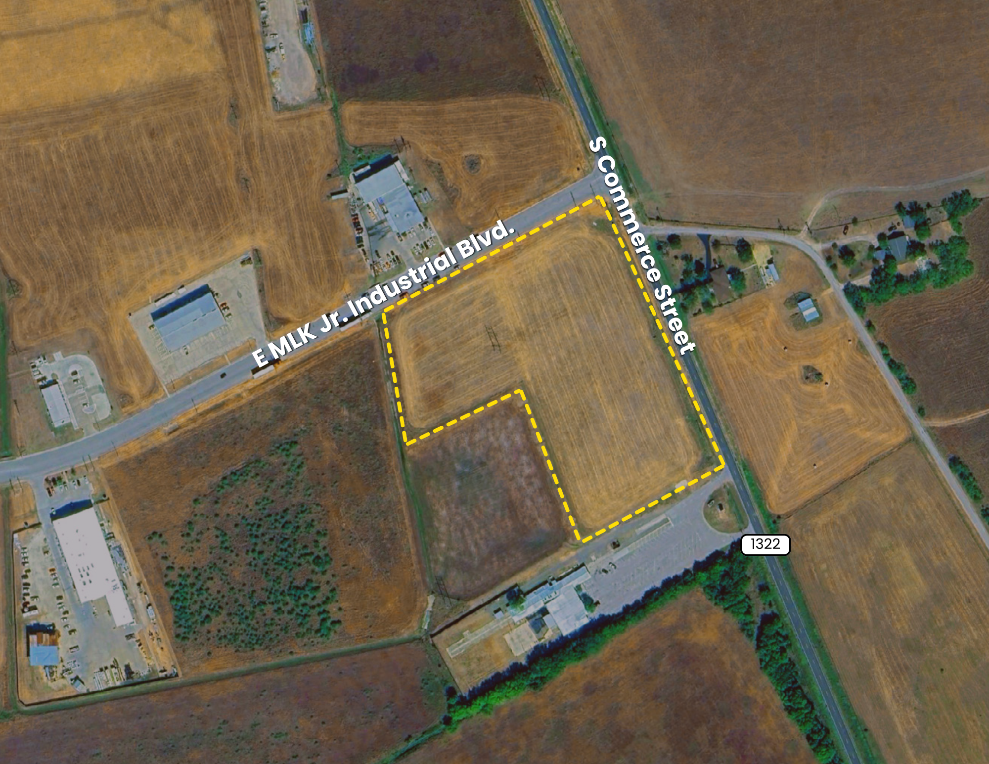 Aerial view of a plot of land outlined with yellow dashed lines near EM LK Jr. Industrial Blvd and S Commerce Street, with surrounding commercial and agricultural areas.