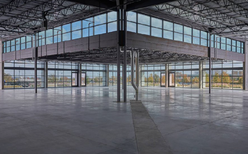 Empty commercial space with large glass windows, high ceiling, exposed metal framework, and polished concrete floor, possibly an office or retail store under construction or renovation.