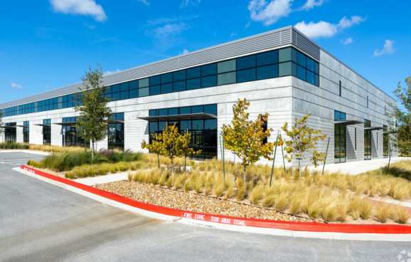 Modern commercial building with glass windows, landscaping, and a fire zone curb in the foreground
