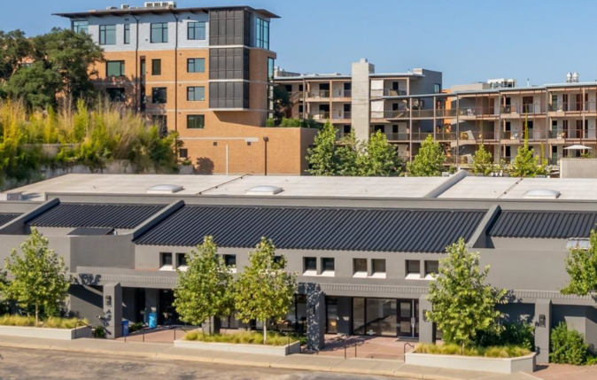 Modern multi-story apartment and commercial buildings, with trees and clear blue sky.