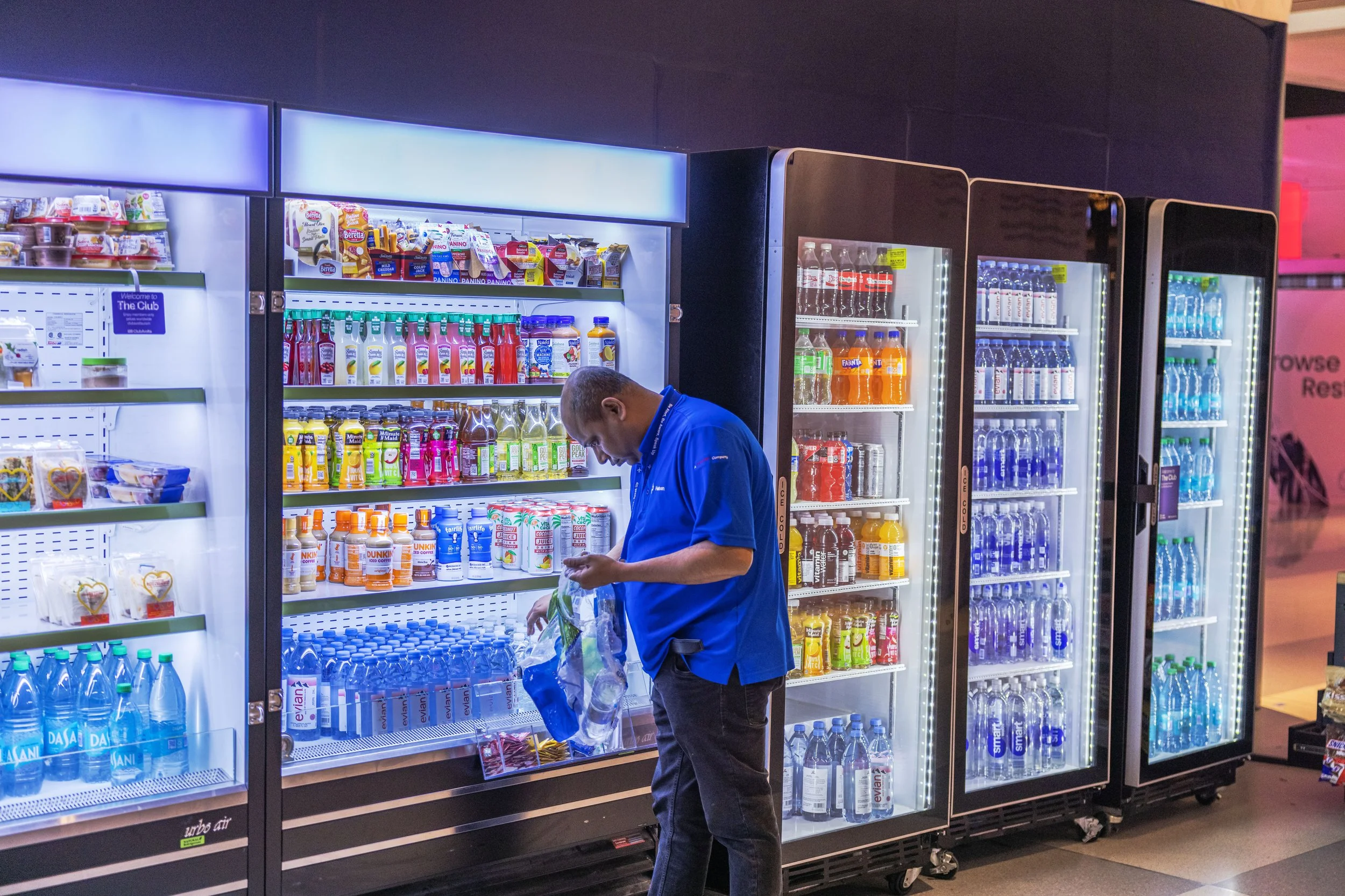 A man in a blue shirt shopping for drinks at a vending machine in a store.