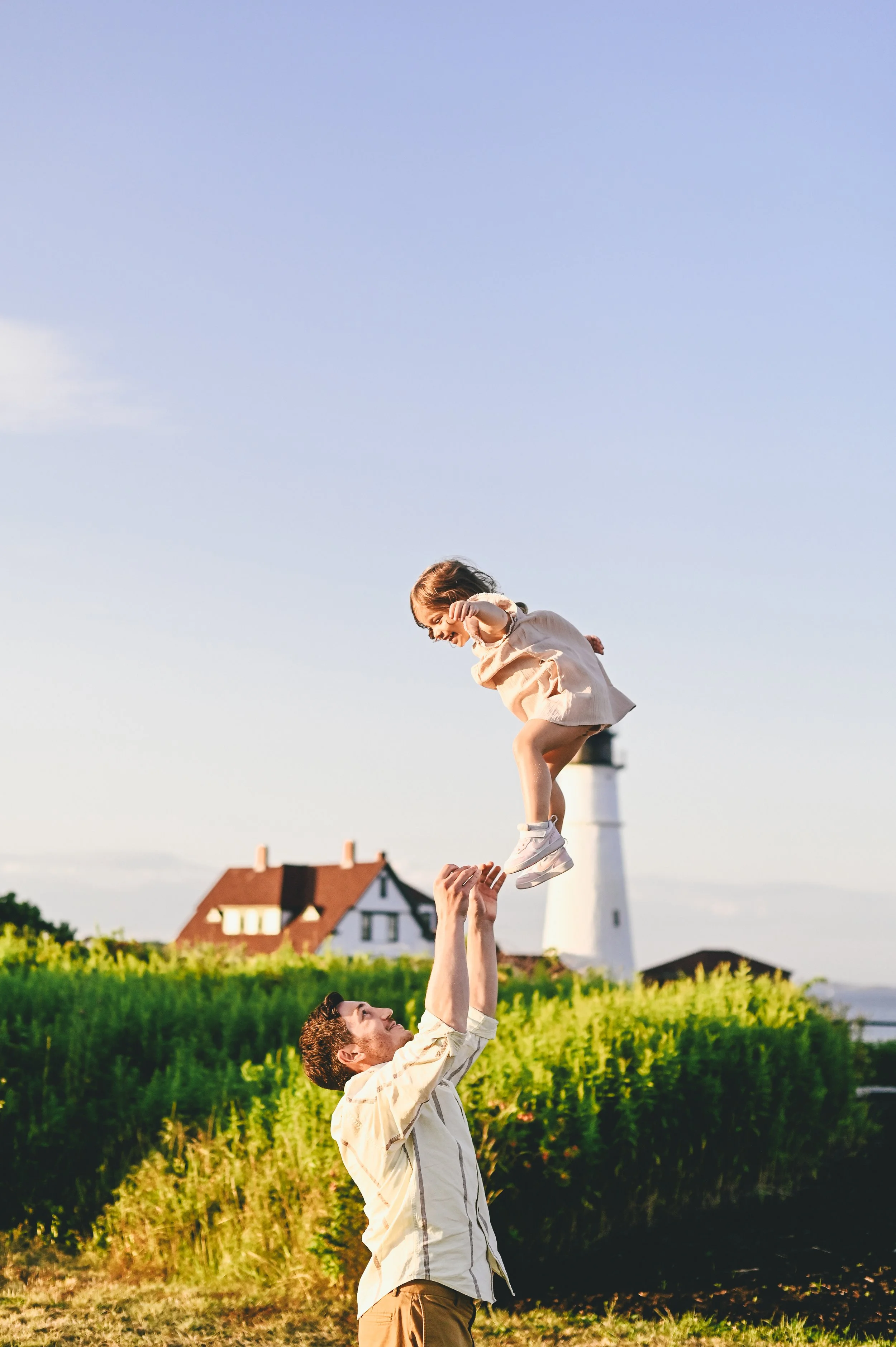 Dad tossing his daughter in the air by a lighthouse in Maine