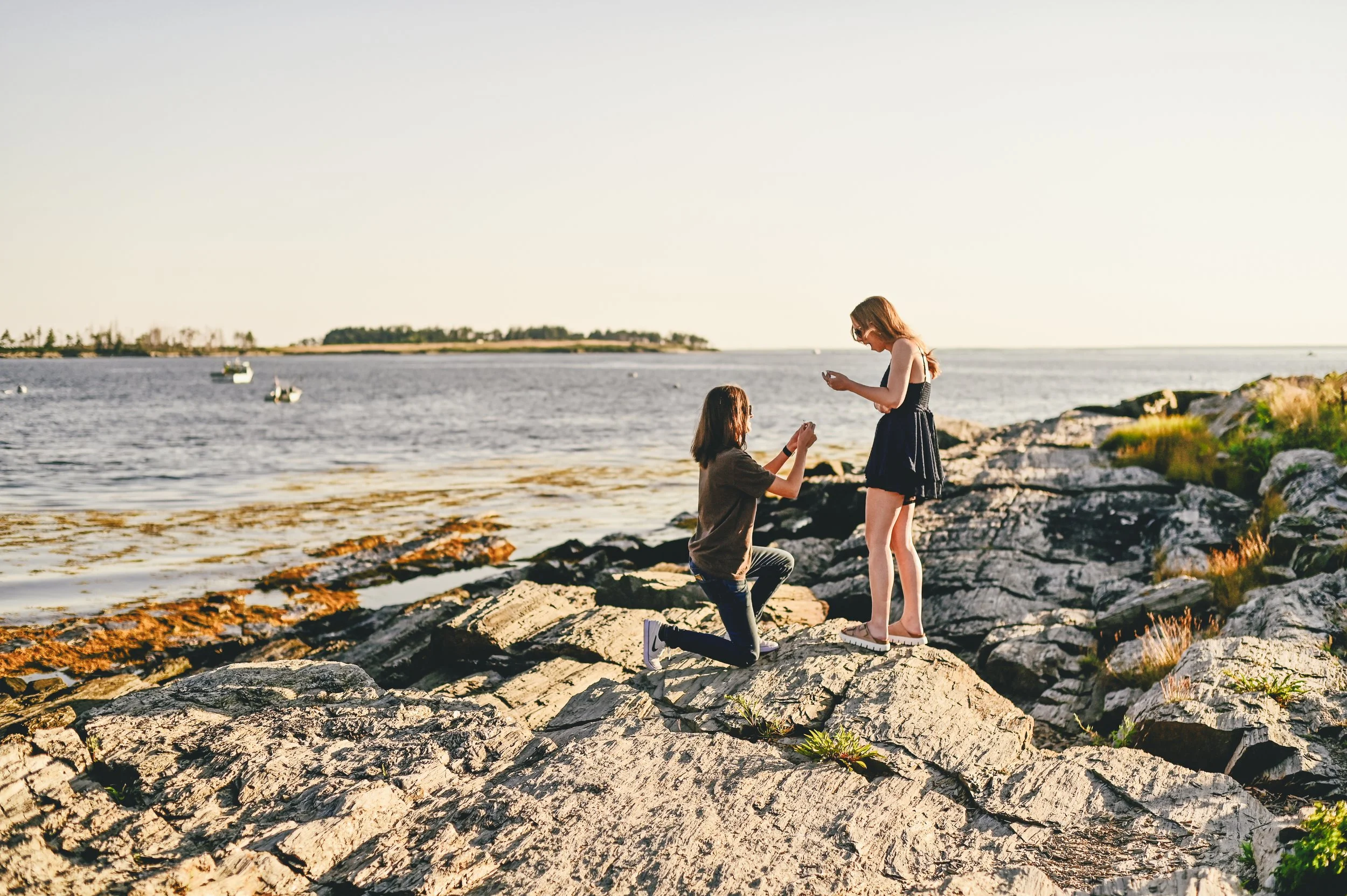 Woman proposes to future bride on coastal rocky beach.