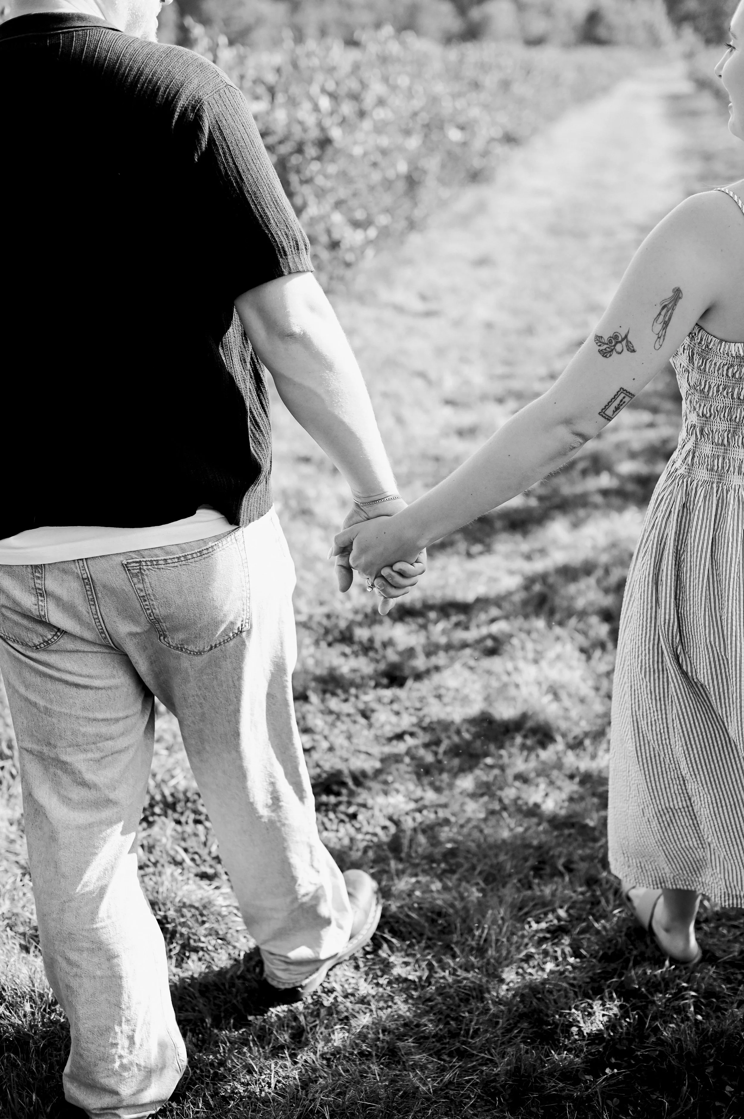 couple with tattoos holding hands in a field during their engagement session