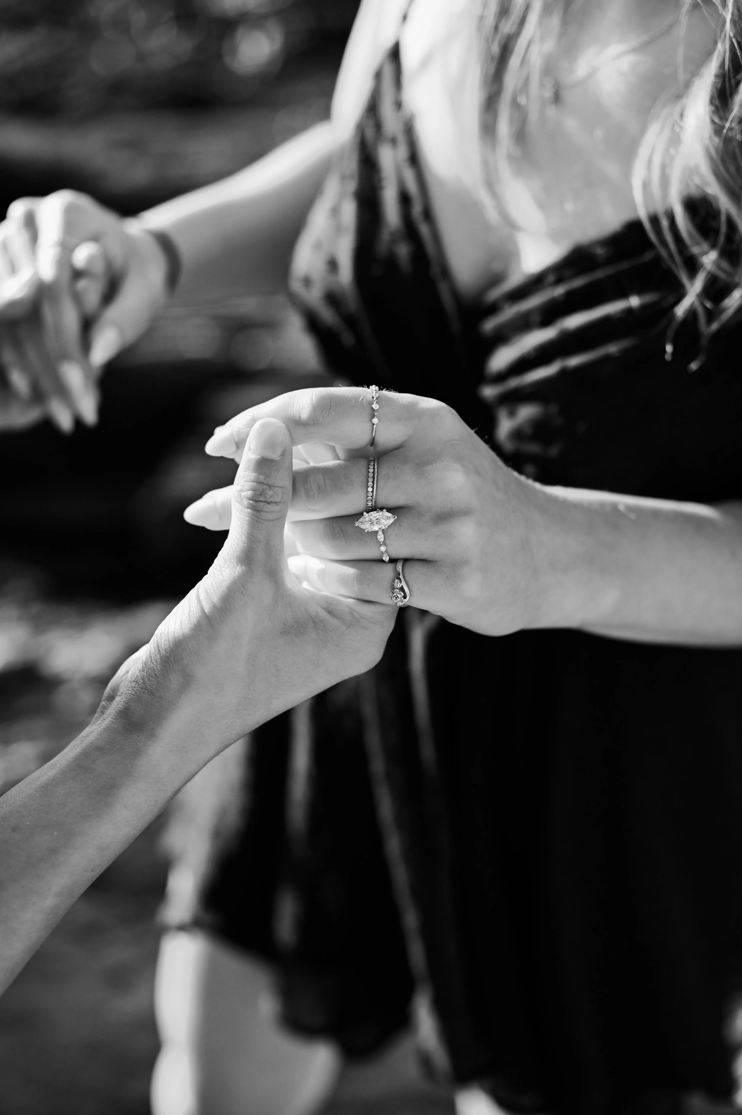 Black white detail shot of future husband and wife holding hands and showing off the engagement ring from recent proposal.