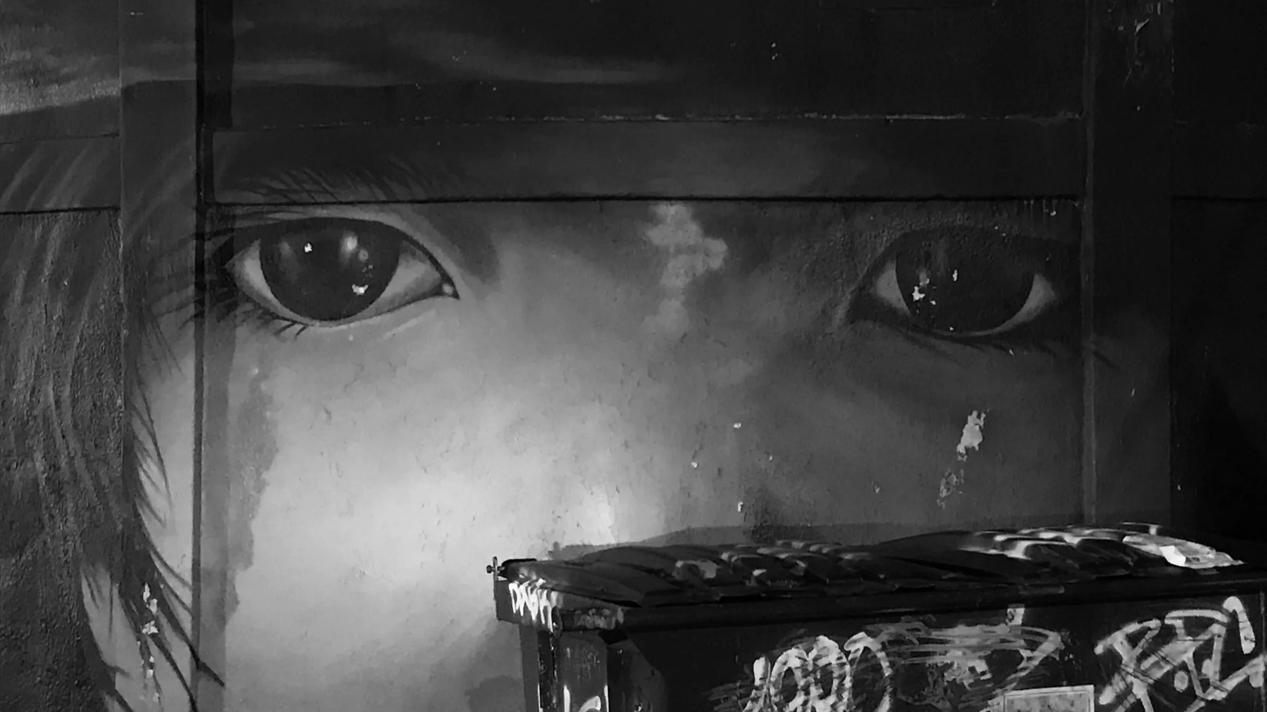 Black-and-white mural of a child's face with large eyes on an urban wall.