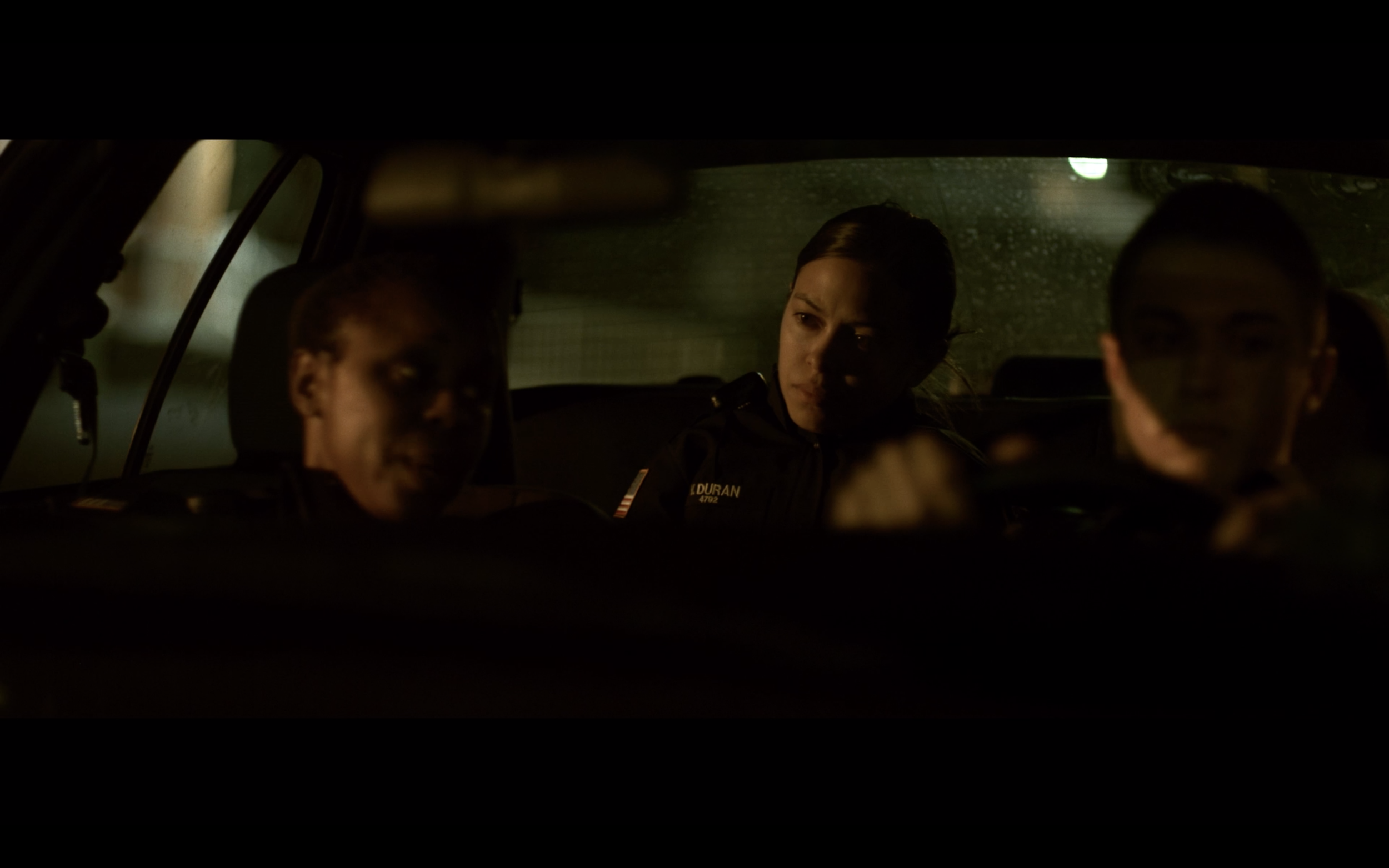 Three women in police uniforms sitting in a vehicle at night, with the interior dimly lit.